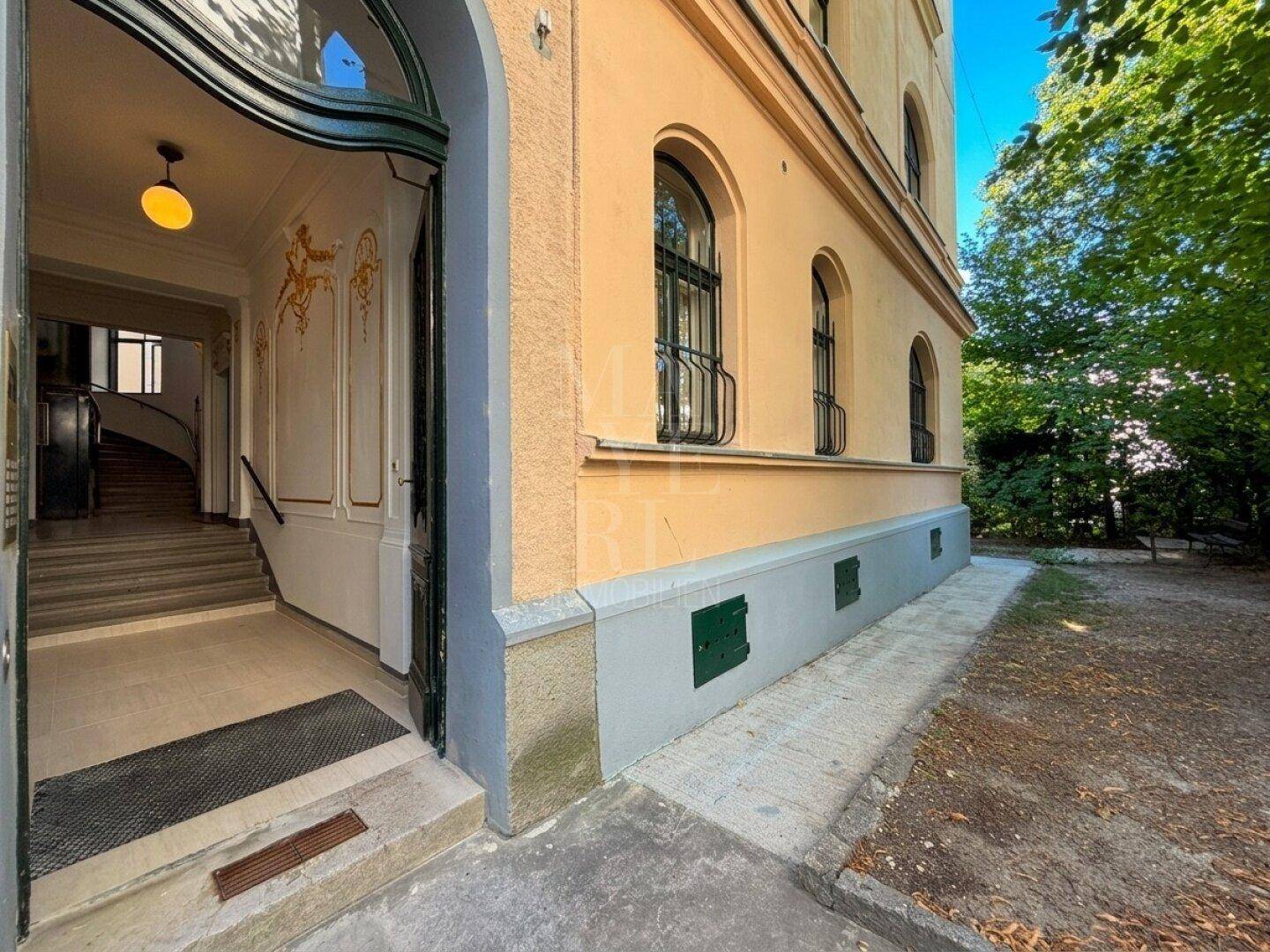 Historisches Gebäude mit eleganter Eingangstür, Bogenfenstern und gepflegter Außenanlage.