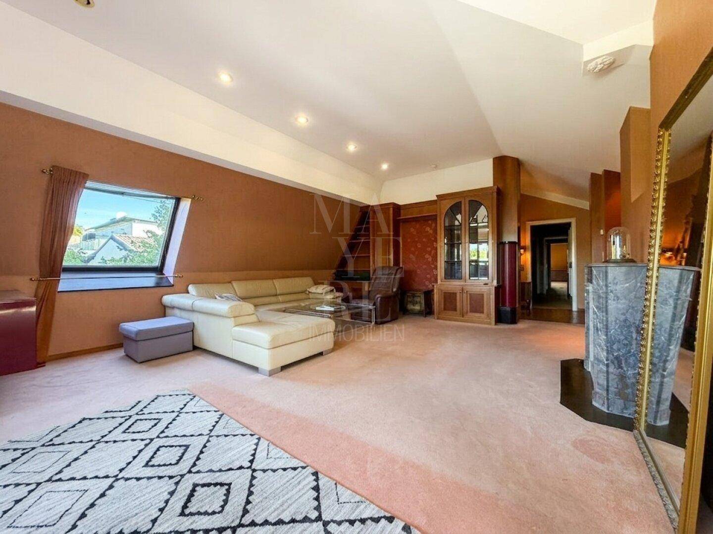 Großzügiges Wohnzimmer mit Teppichboden, beiger Couch und einem Kamin in warmer Farbgebung.