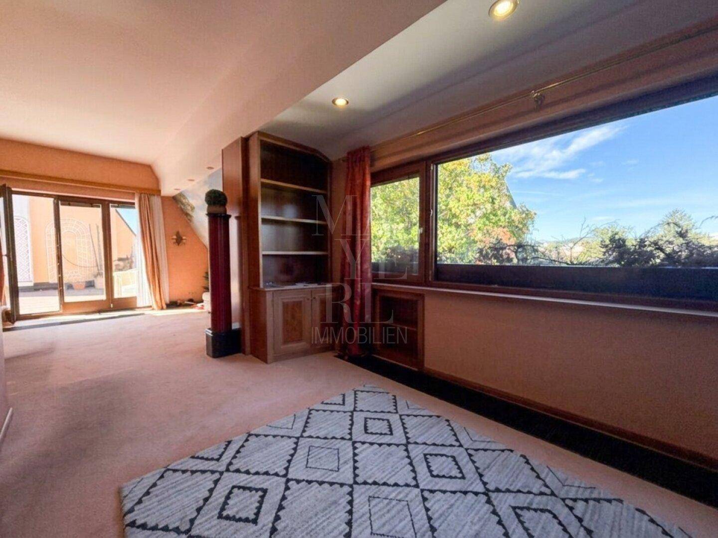 Helles Wohnzimmer mit Teppichboden, großem Fenster und Zugang zu einer Außenterrasse.