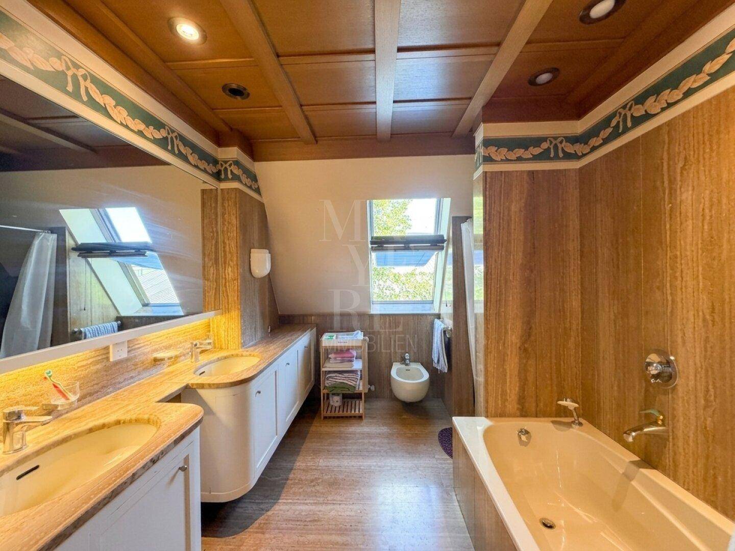 Geräumiges Badezimmer mit Doppelwaschbecken, Badewanne, Bidet und Holzelementen.