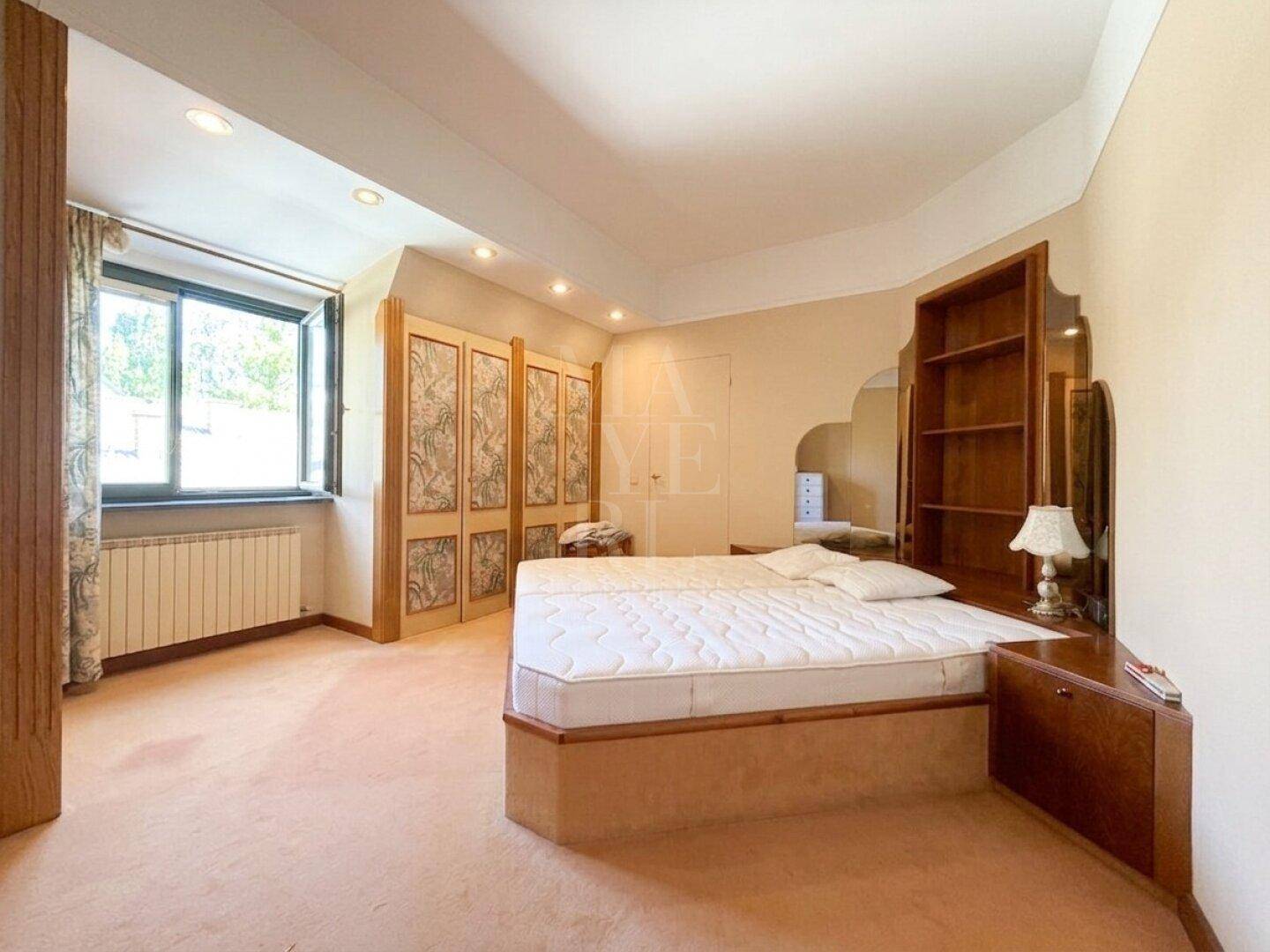 Schlafzimmer mit Teppichboden, großem Fenster und Einbauschränken in warmen Farbtönen.