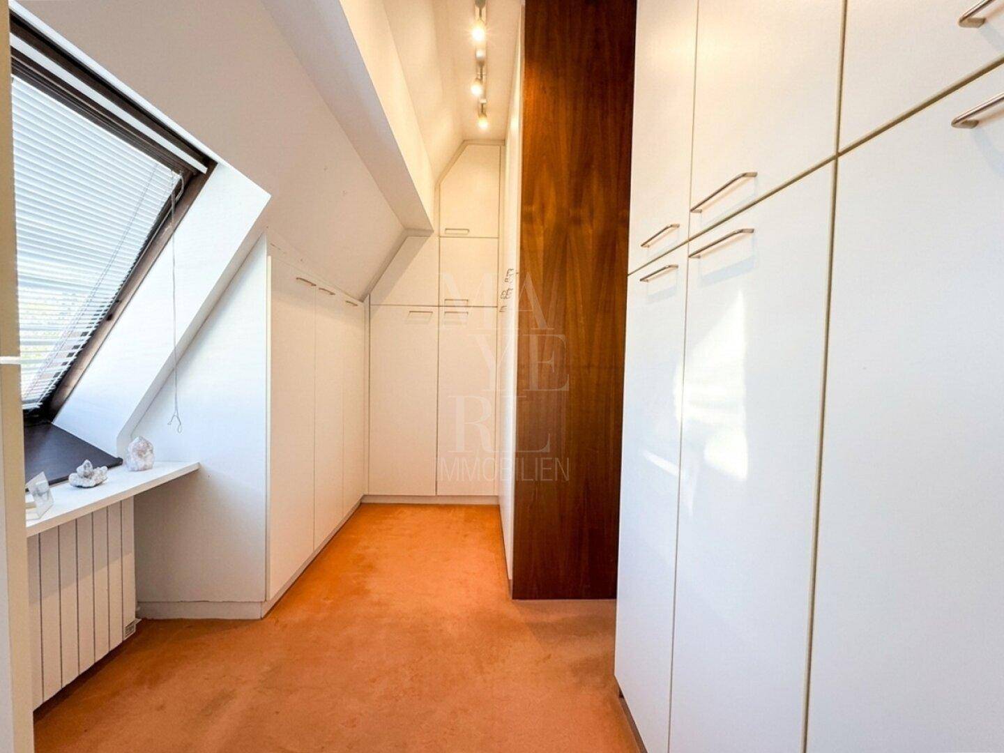 Langer Flur mit Einbauschränken, Teppichboden und Dachfenster für zusätzliche Helligkeit.