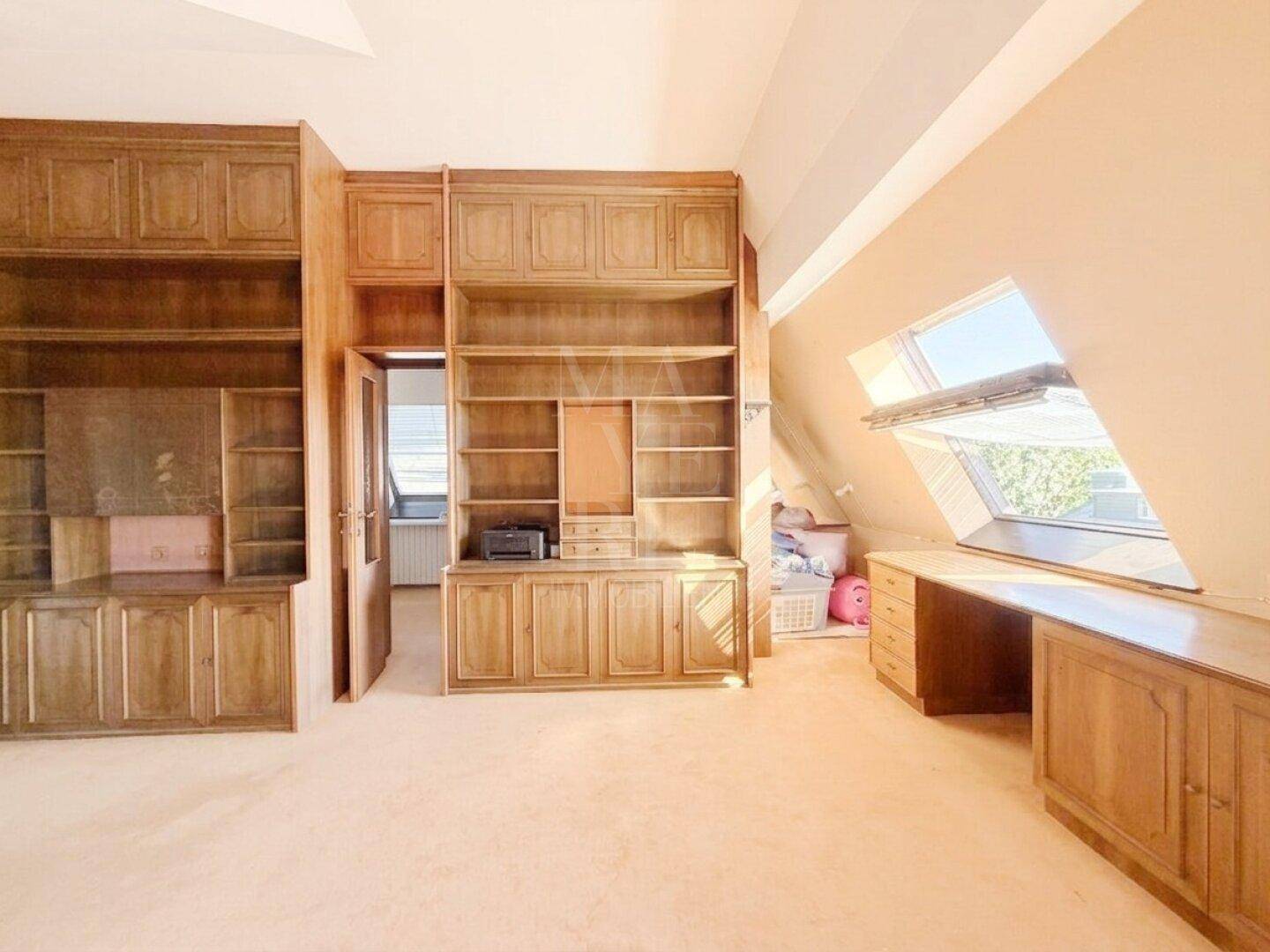 Arbeitszimmer mit umfangreichen Holzregalen, Teppichboden und Dachfenster für natürliches Licht.