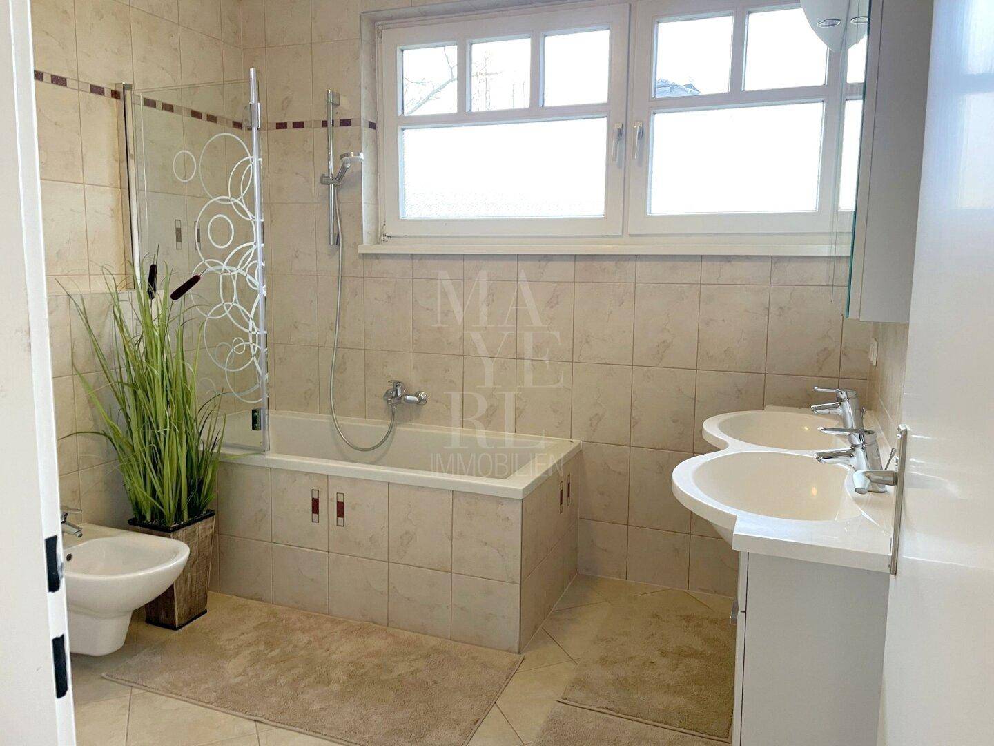 Helles Badezimmer mit Badewanne, Duschfunktion, Doppelwaschbecken, Bidet und Fenster.