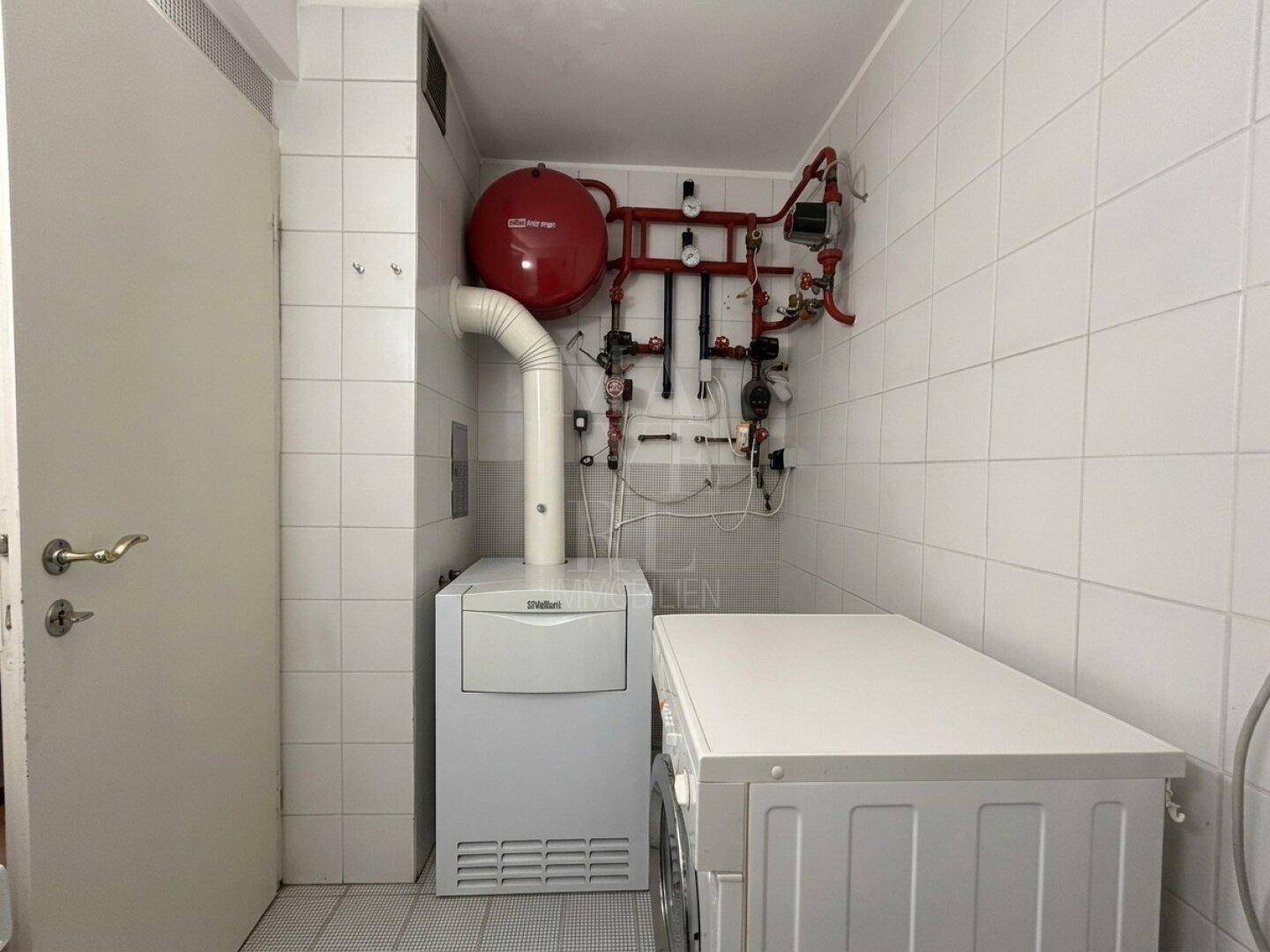 Hauswirtschaftsraum mit Heizungsanlage, Warmwasserspeicher und Waschmaschine, komplett gefliest in Weiß.
