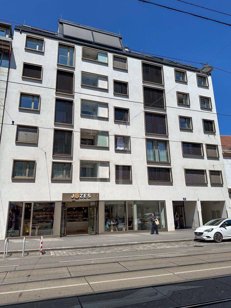 Moderne Gebäudefassade mit Wohnungen und Geschäftsräumen im Erdgeschoss an einer belebten Straße.