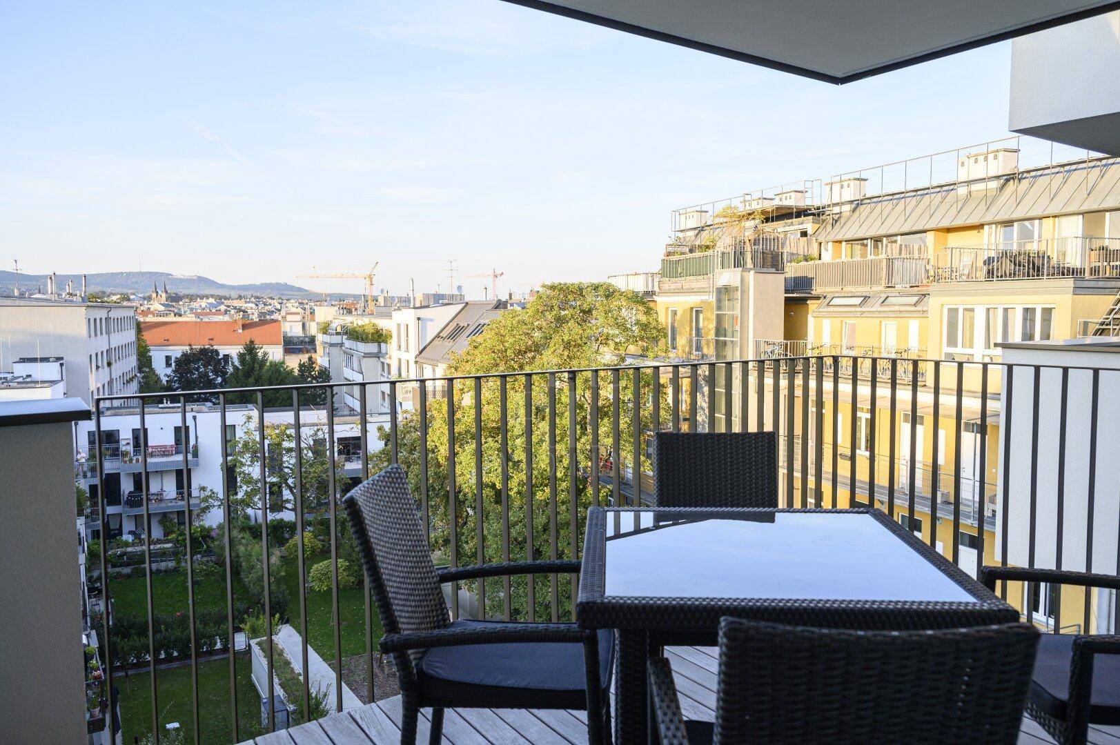 Möblierter Balkon mit weitreichendem Blick über die Stadt und umliegende Gebäude bei Tageslicht.