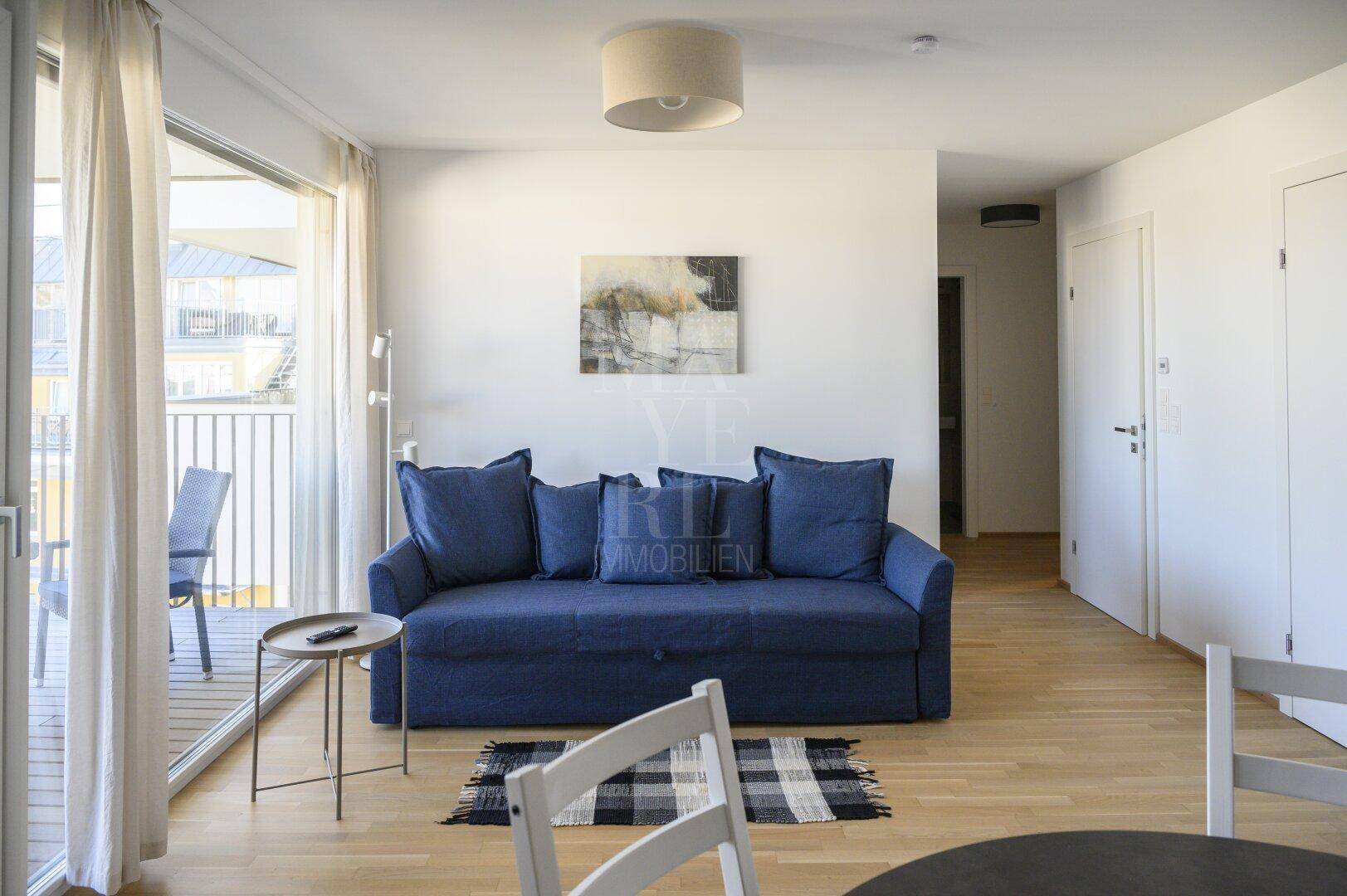Gemütlicher Wohnbereich mit blauem Sofa, Holzboden und direktem Zugang zum Balkon.