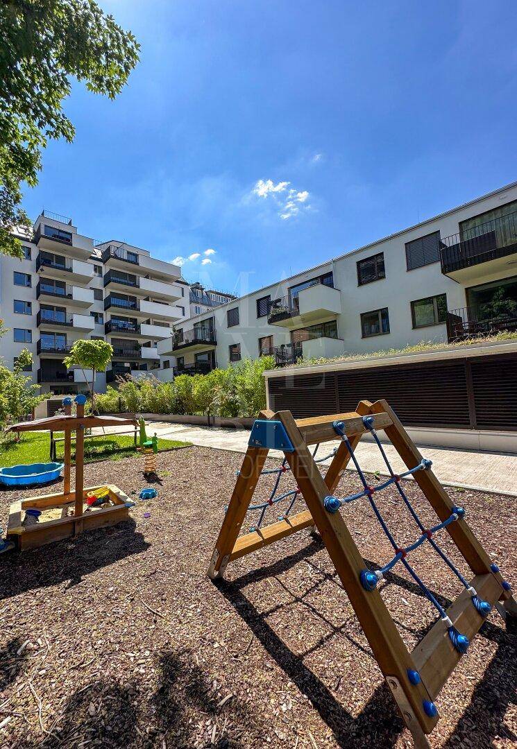 Kinderspielplatz im Freien mit Klettergerüst und Sandkasten vor modernen Wohngebäuden.