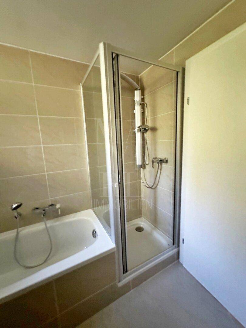 Badezimmer mit Badewanne, Duschkabine und beigefarbenen Fliesen an Wänden und Boden.