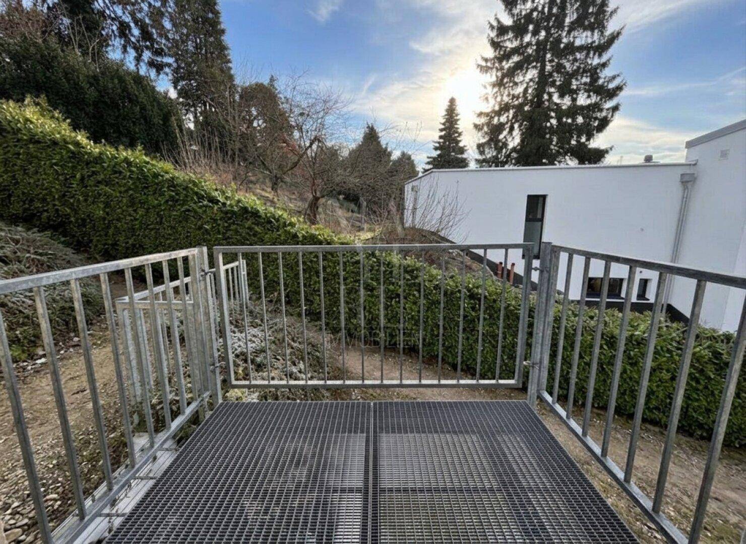 Kleiner Balkon mit Metallgitterboden und Blick auf die grüne Umgebung und das Gebäude.