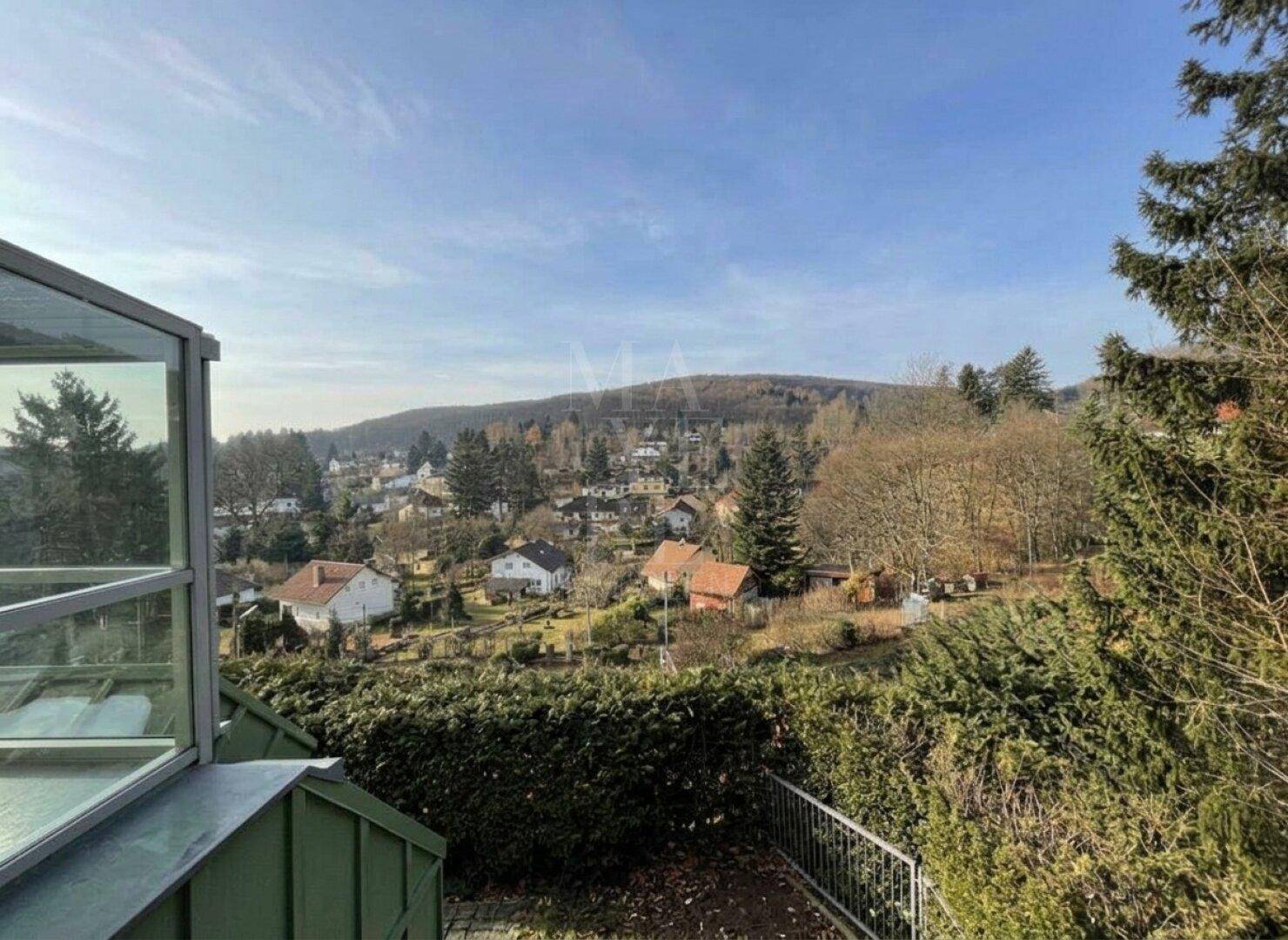 Weitläufiger Blick über eine grüne Hügellandschaft mit Häusern unter blauem Himmel.