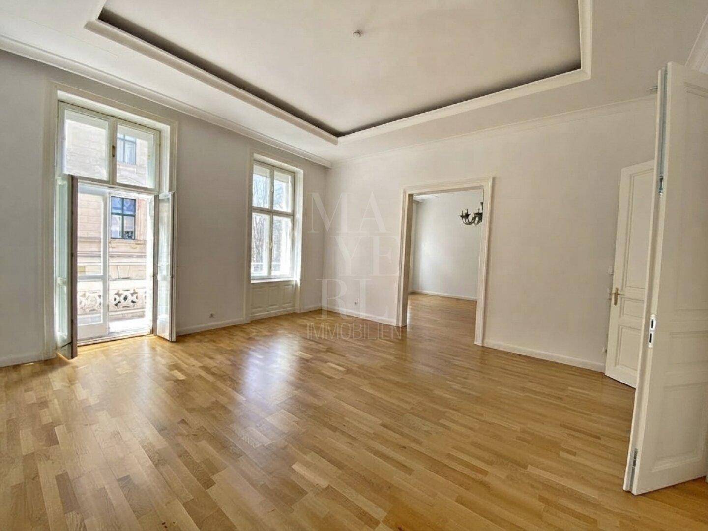 Helles Wohnzimmer mit Eichenparkett, hohen Decken und Zugang zu einem französischen Balkon.