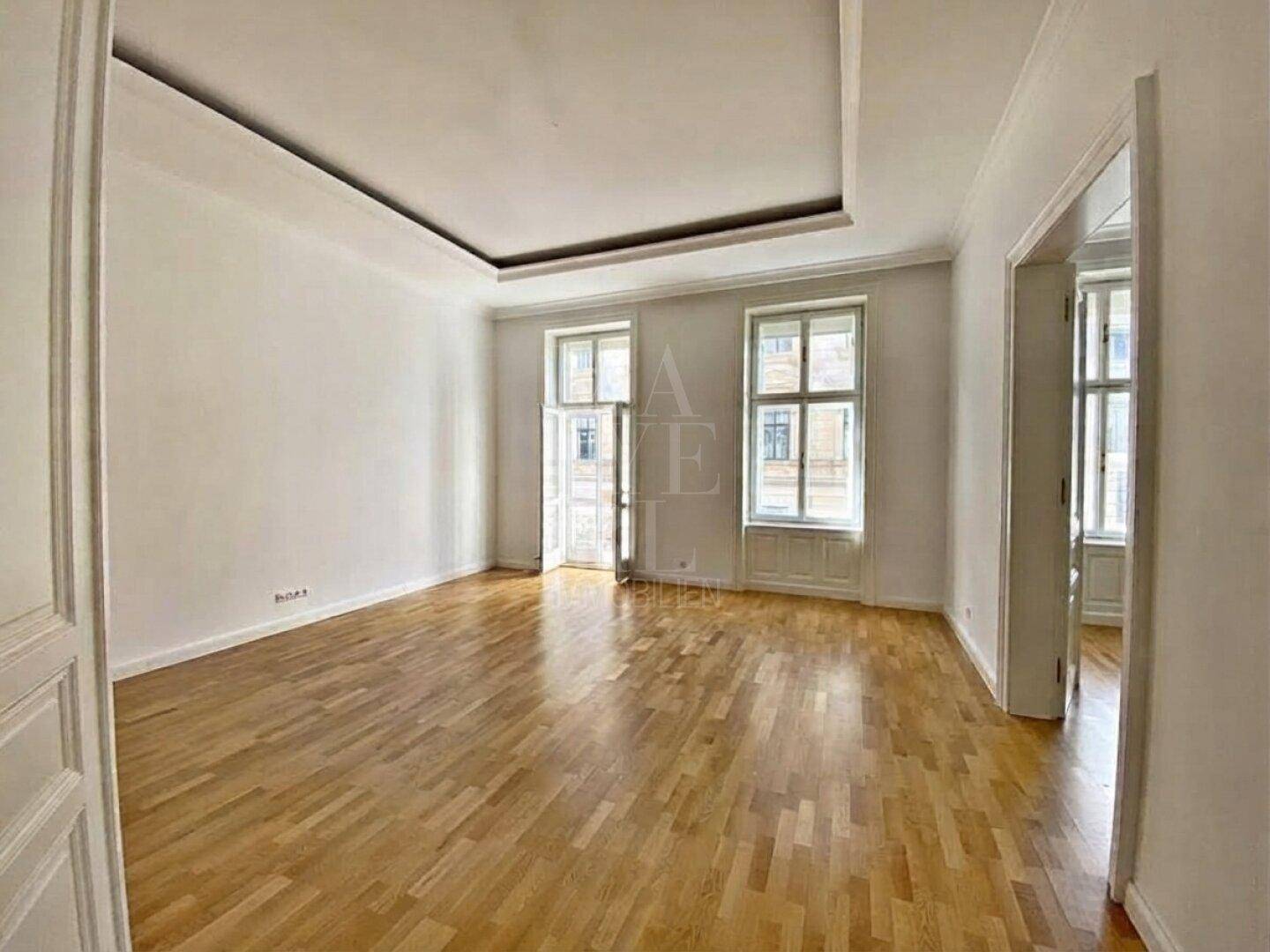Lichtdurchflutetes Wohnzimmer mit klassischem Parkettboden, hohen Decken und großen Fenstern.