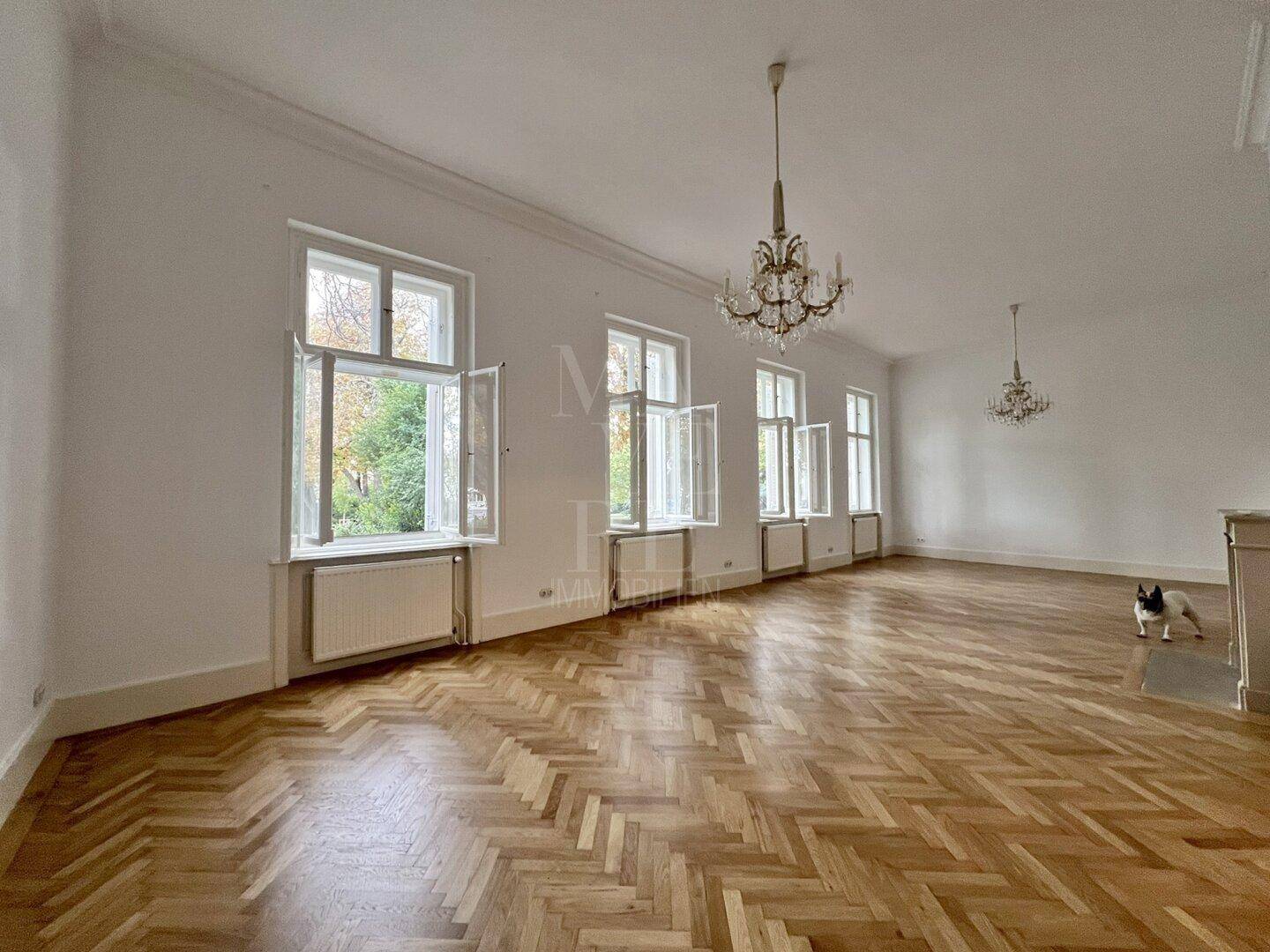 Helles Wohnzimmer mit klassischem Fischgrätparkett und vielen Fenstern, die eine lichtdurchflutete Atmosphäre schaffen.