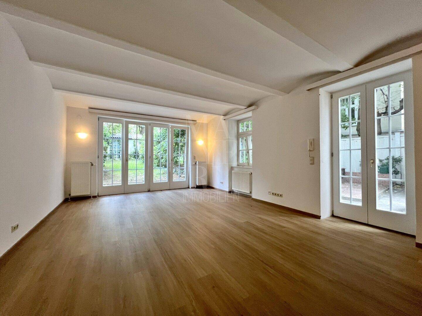 Helles Zimmer mit Holzboden, sichtbaren Deckenbalken und direktem Zugang zum grünen Garten.