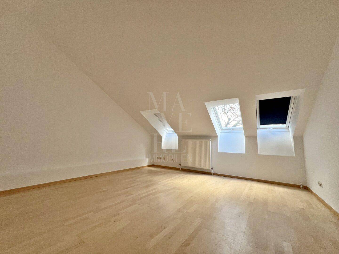 Lichtdurchflutetes Dachzimmer mit Holzboden und drei Dachfenstern, die eine helle Atmosphäre schaffen.
