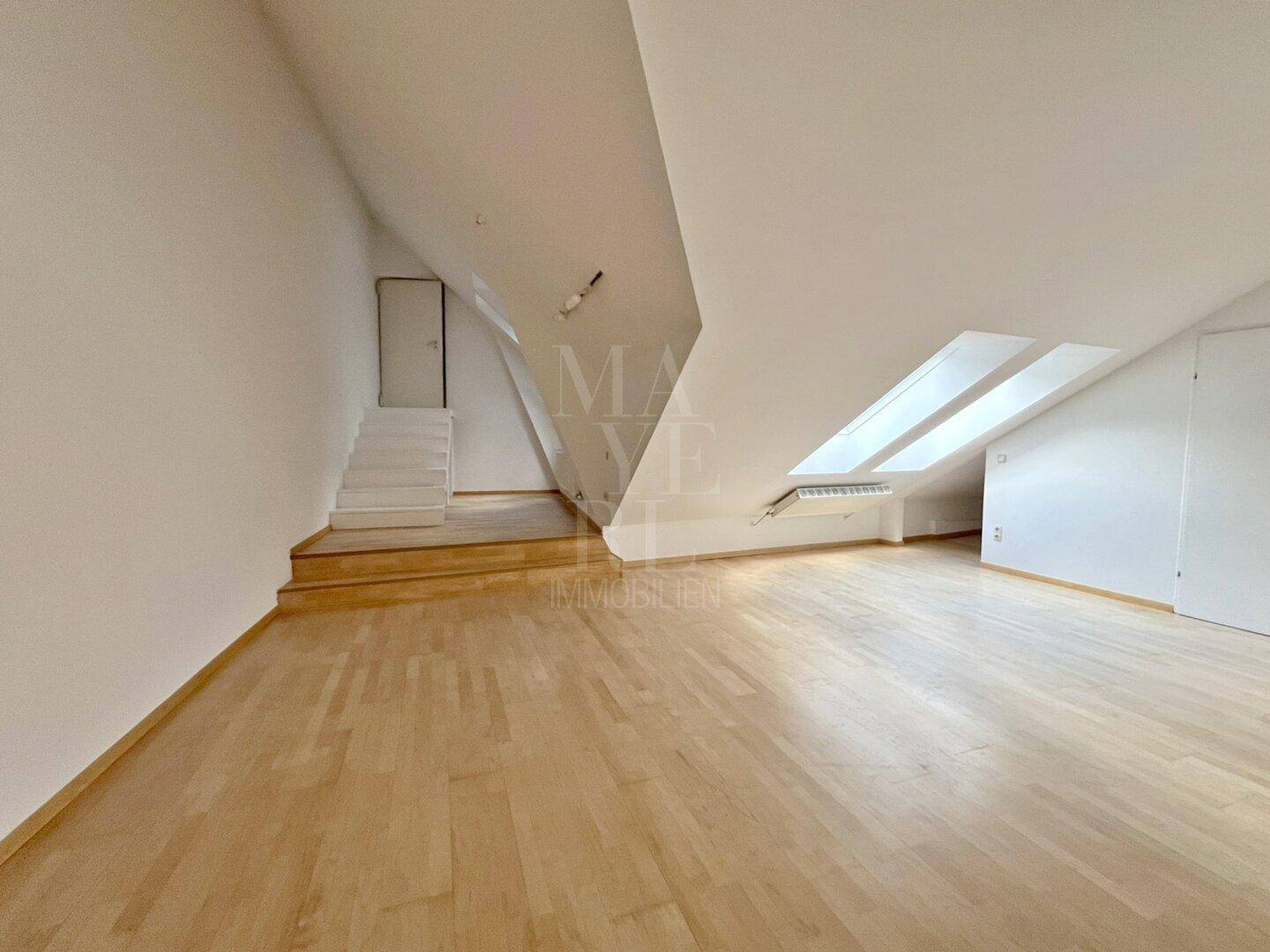 Geräumiges Dachgeschoss mit Holzboden, schrägen Wänden und mehreren Dachfenstern, die Helligkeit spenden.