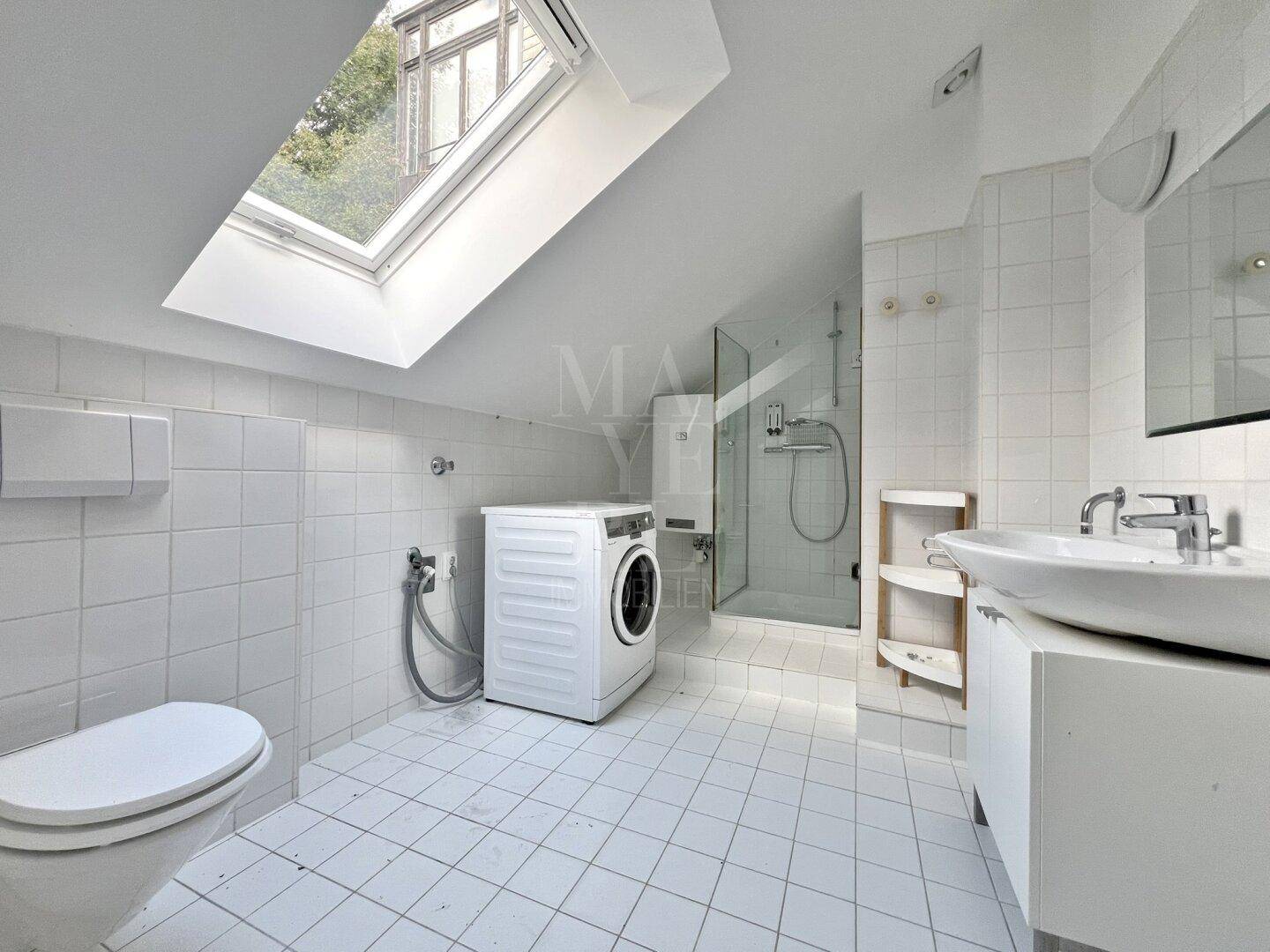 Dachgeschoss-Badezimmer mit großem Dachfenster, Dusche, WC und praktischer Waschmaschine.