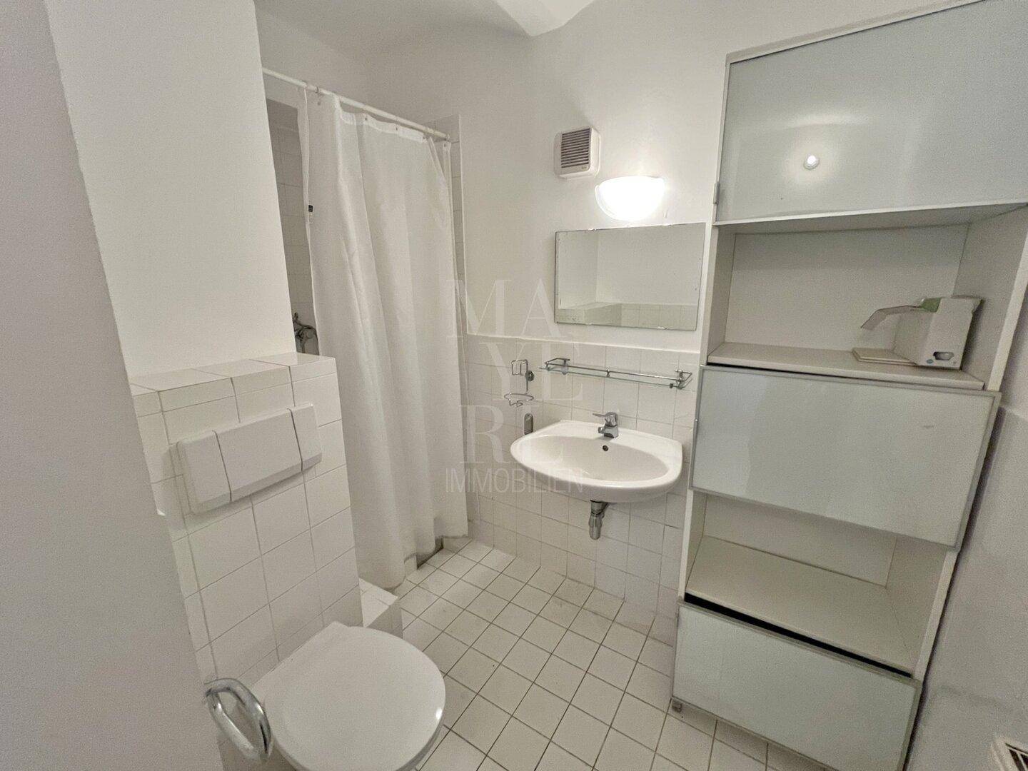 Kleines Badezimmer mit weißen Fliesen, WC, Waschbecken und einem praktischen Duschvorhang.