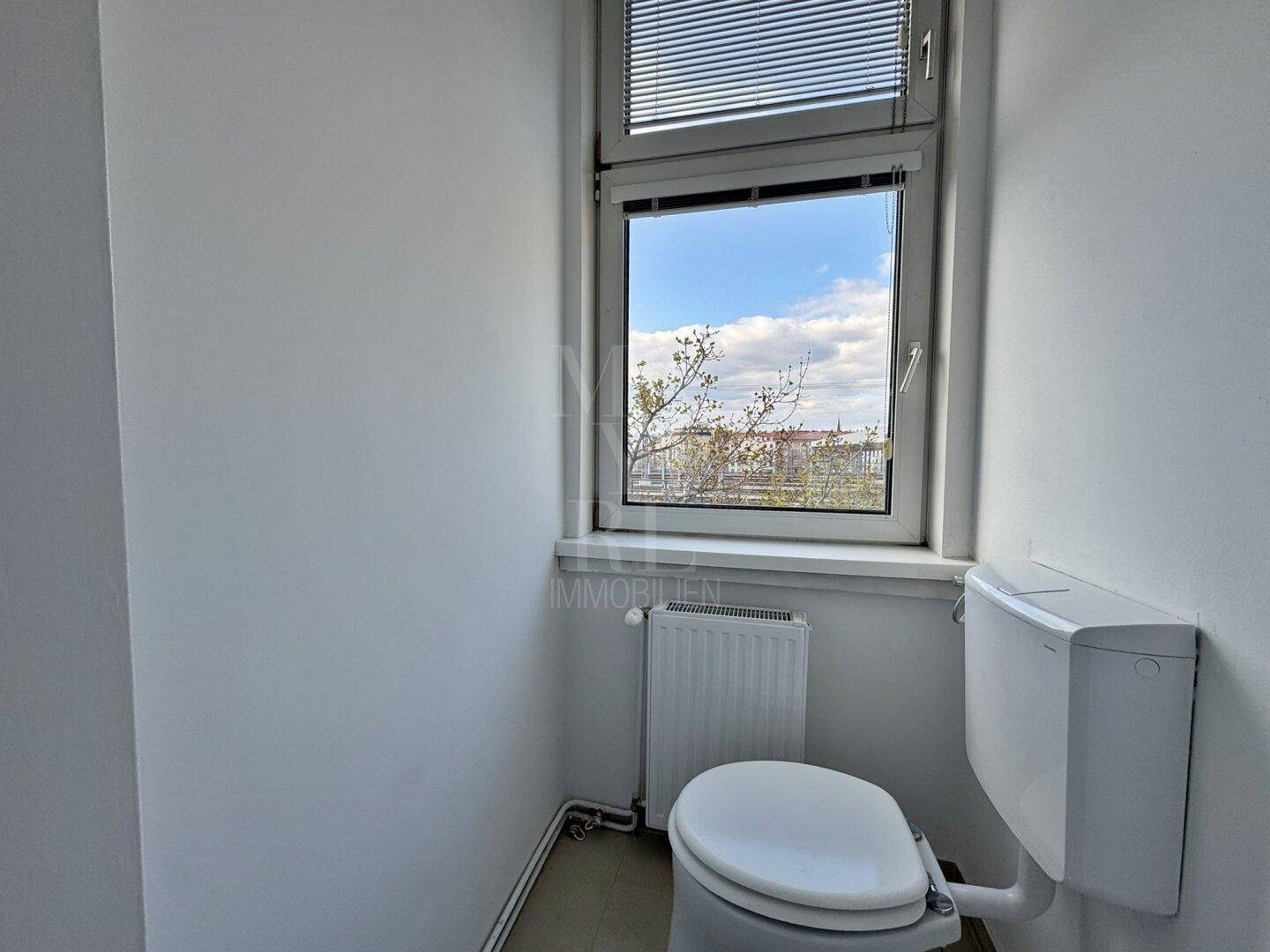 Separates WC mit Toilette und einem Fenster für natürliche Belüftung und Tageslicht.