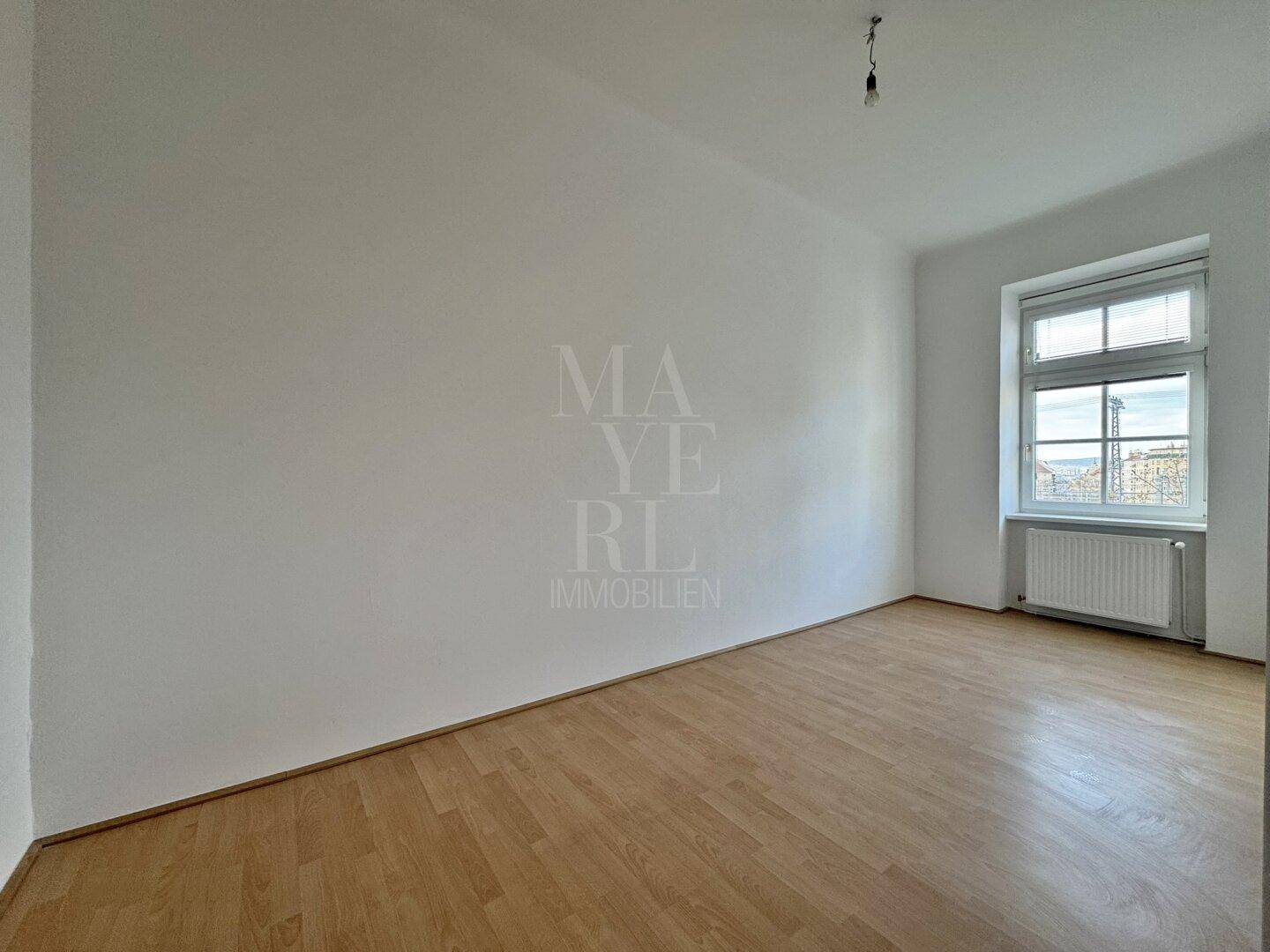 Ruhiges, unmöbliertes Zimmer mit Parkettboden und einem großen Fenster, ideal als Schlafzimmer.