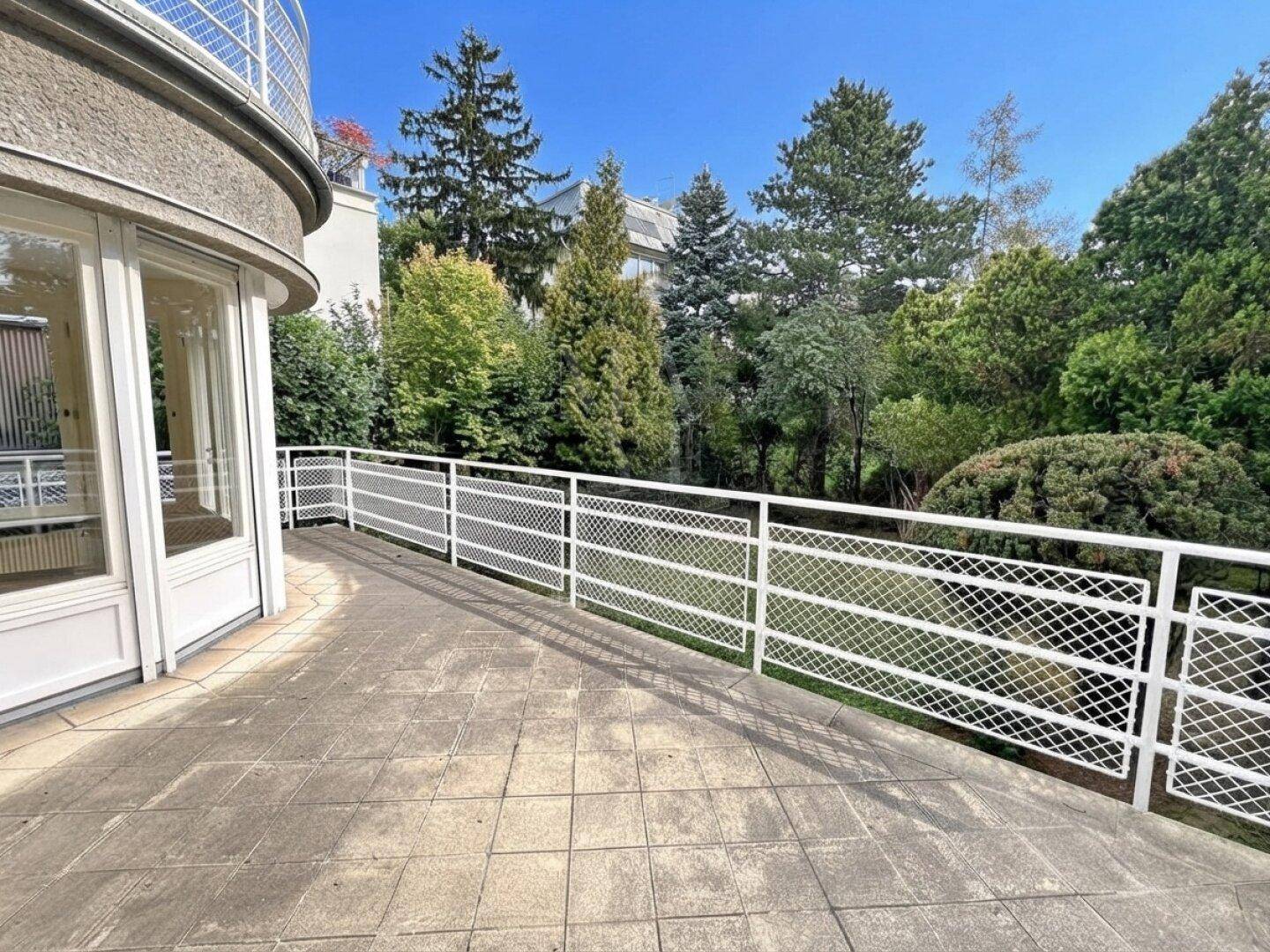 Geräumige Terrasse mit Fliesenboden und weißem Geländer, umgeben von viel Grün.