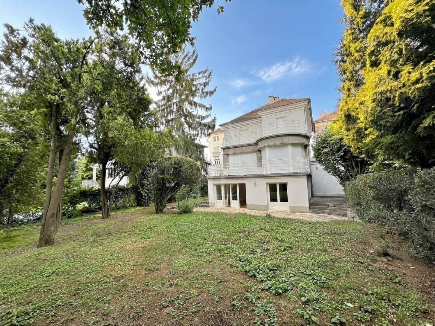 Großer Garten mit altem Baumbestand und Blick auf die weiße Villa mit Balkon und Terrasse.