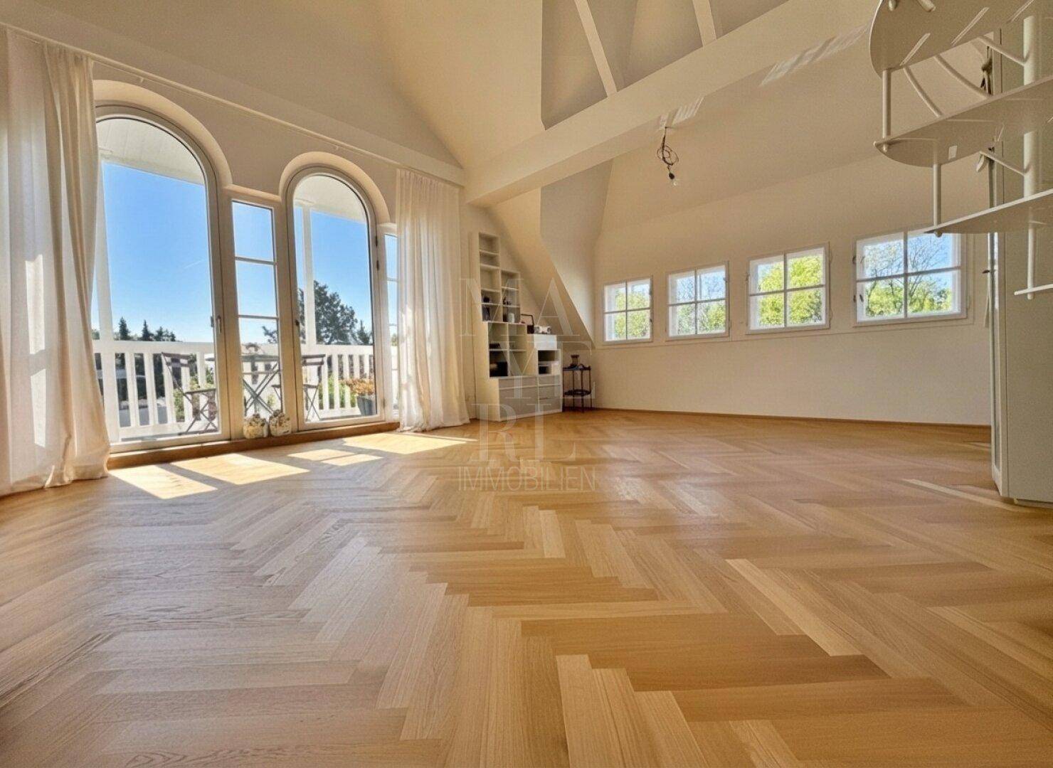 Weitläufiger, heller Raum mit Fischgrätparkett, hohen Decken und Zugang zum Balkon.