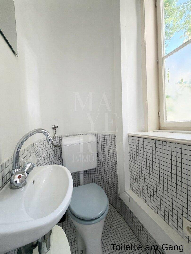 Kompakte Gästetoilette mit Fenster, kleinem Waschbecken und Fliesen im Schachbrettmuster an den Wänden.
