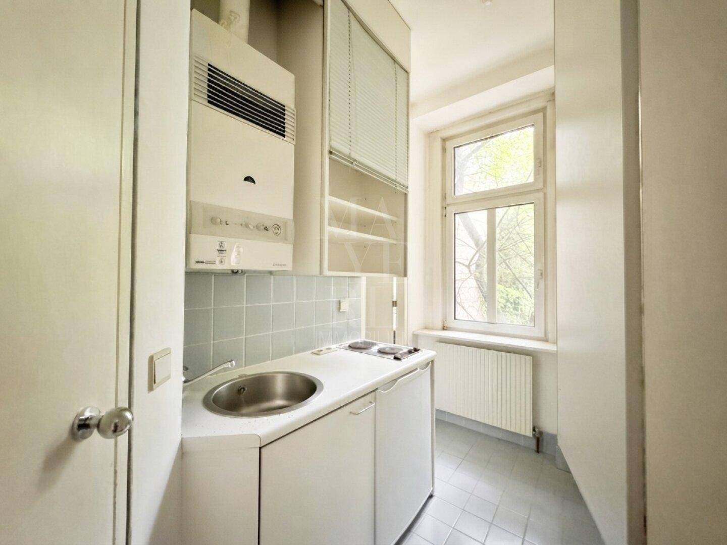 Kompakte Küchenzeile mit Spüle, Kochfeld und einem Wandheizkessel, ideal für kleine Wohnbereiche.