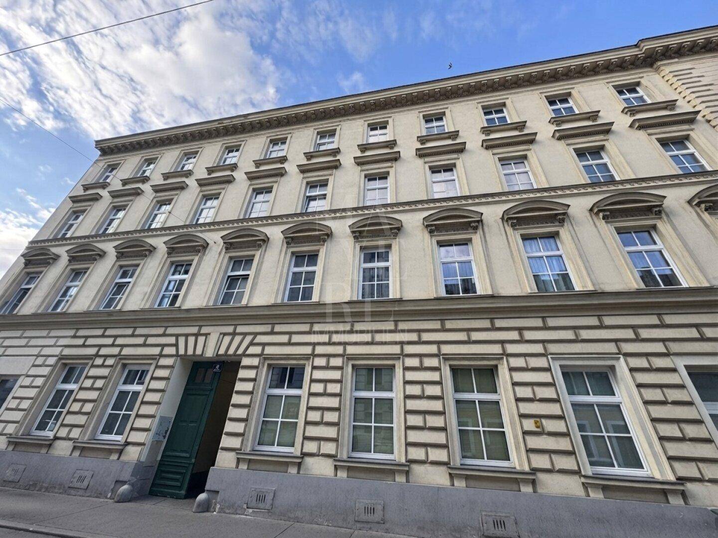 Klassische Fassade eines Altbaus mit zahlreichen Fenstern und architektonischen Details unter blauem Himmel.