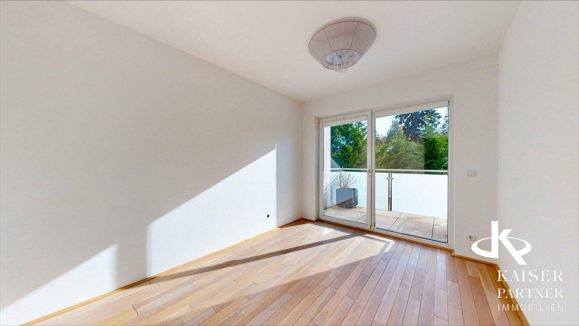 Heller Raum mit Holzboden und großer Glasfront, die Zugang zu einem sonnigen Balkon bietet.