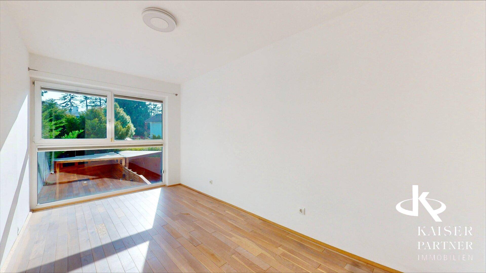 Geräumiger Raum mit Holzboden und großer Fensterfront, die viel Tageslicht hereinlässt.