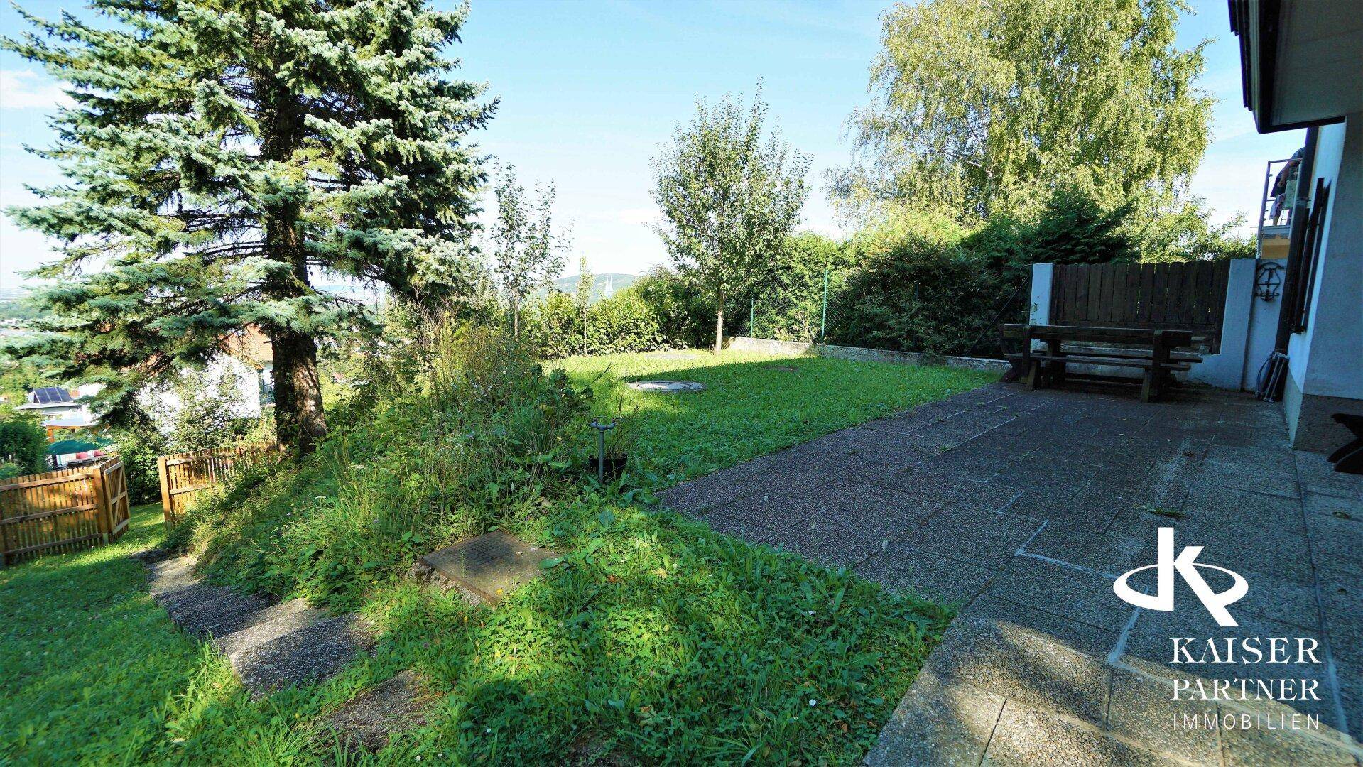 Gepflegter Garten mit Rasenfläche und gepflasterter Terrasse, ideal für entspannte Stunden im Freien.