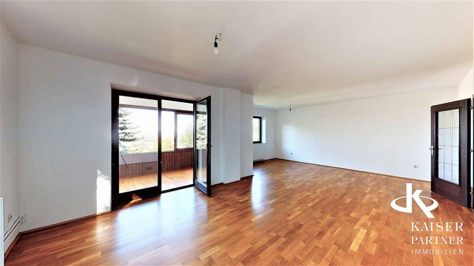 Helles Wohnzimmer mit Parkettboden und Zugang zu einem Balkon, bietet viel natürliches Licht.