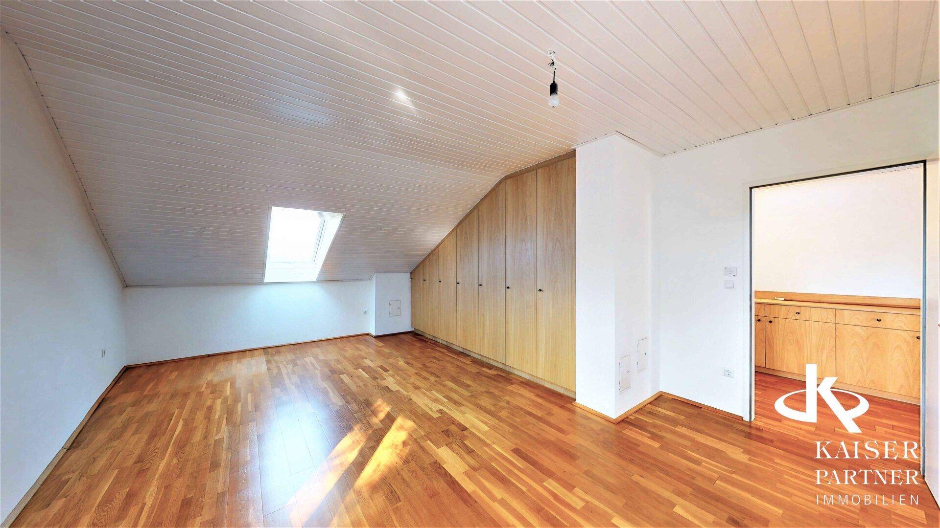 Geräumiges Dachzimmer mit Holzdecken, Einbauschränken und Parkettboden, bietet viel Stauraum.