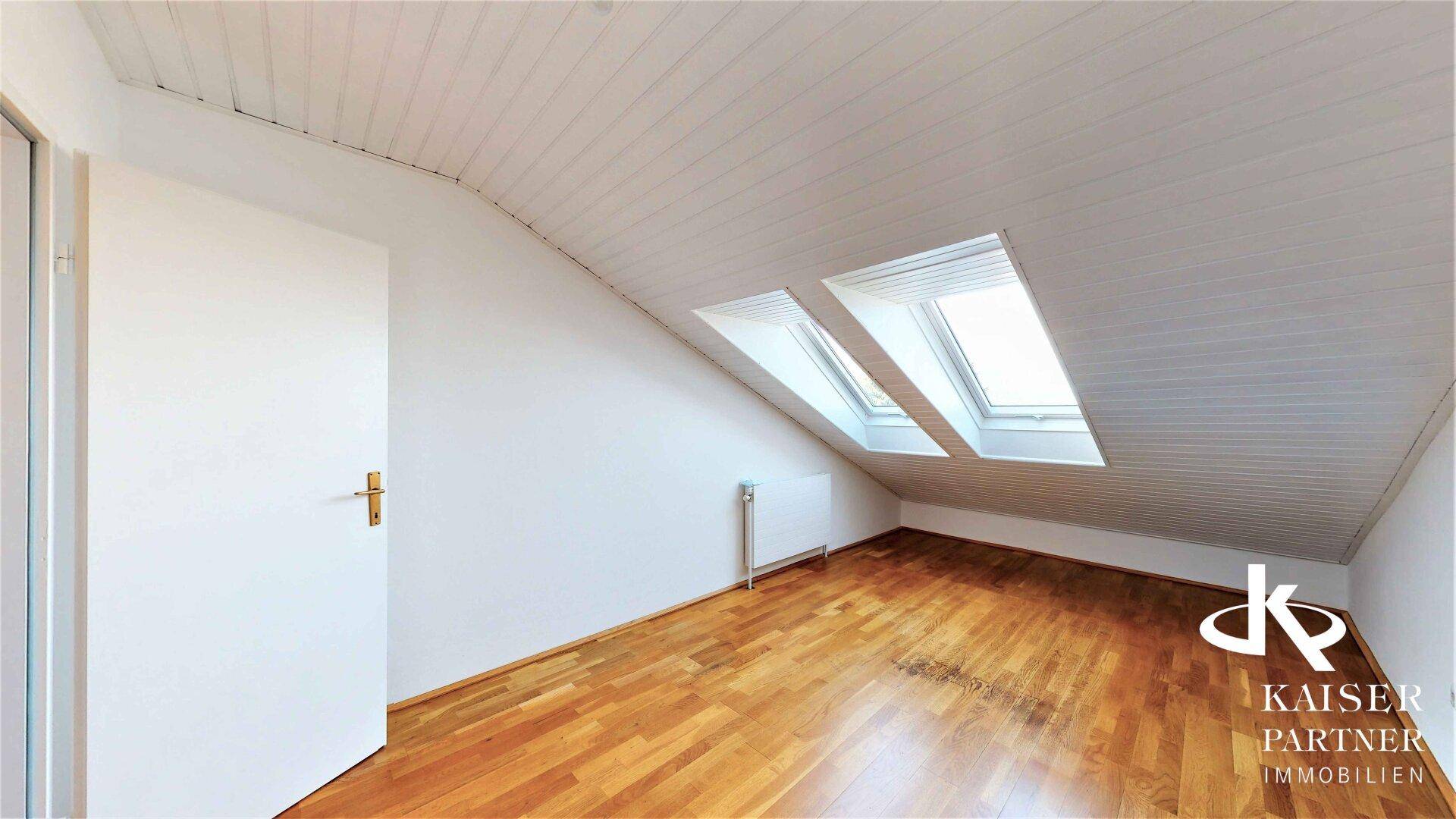 Helles Dachzimmer mit Parkettboden und zwei Dachfenstern, die den Raum mit Tageslicht füllen.