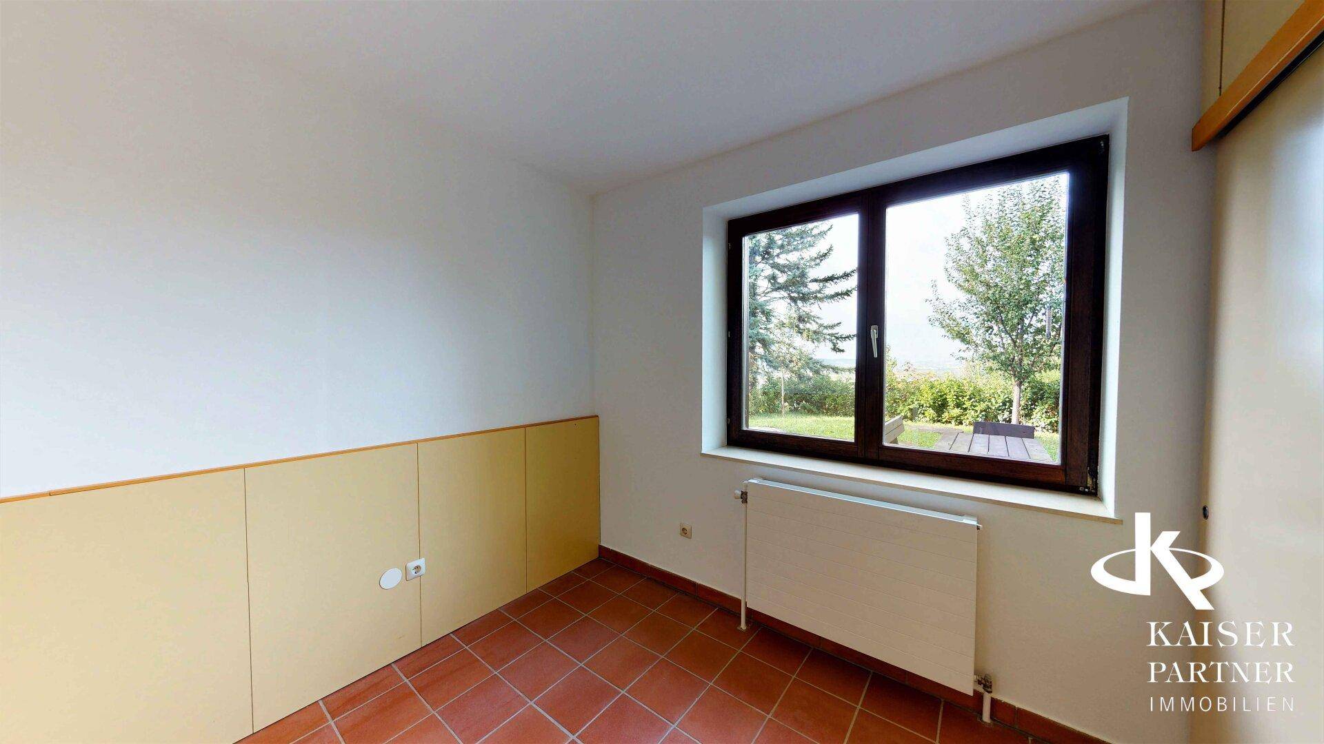 Zimmer mit Terrakotta-Fliesenboden und einem Fenster, das den Blick ins Grüne ermöglicht.