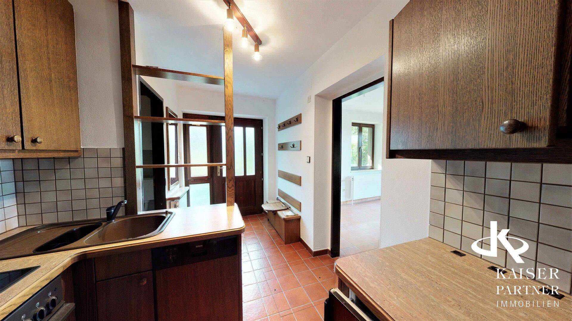 Blick auf den Eingangsbereich mit Küchenzeile, Garderobe und Terrakotta-Fliesenboden.