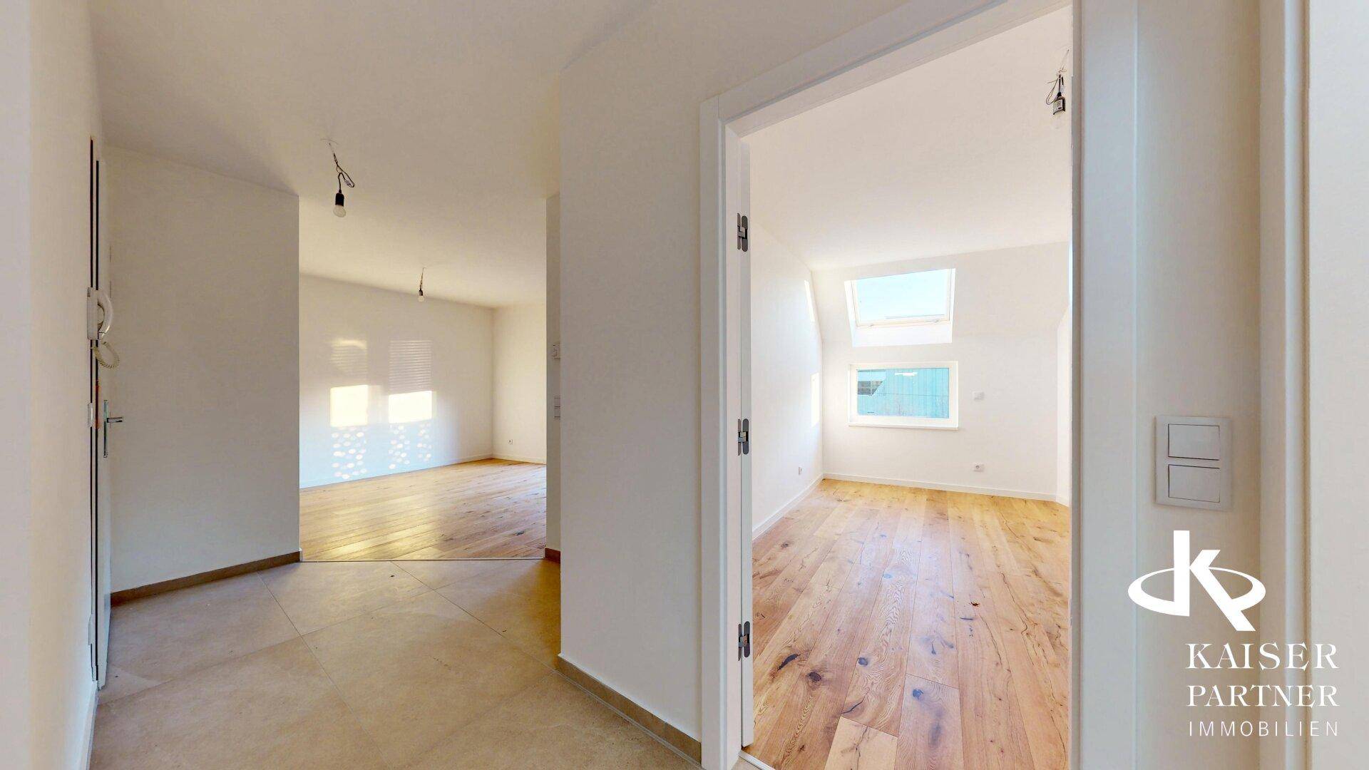 Flur mit Fliesenboden und offener Tür zu einem weiteren hellen Zimmer mit Holzboden.