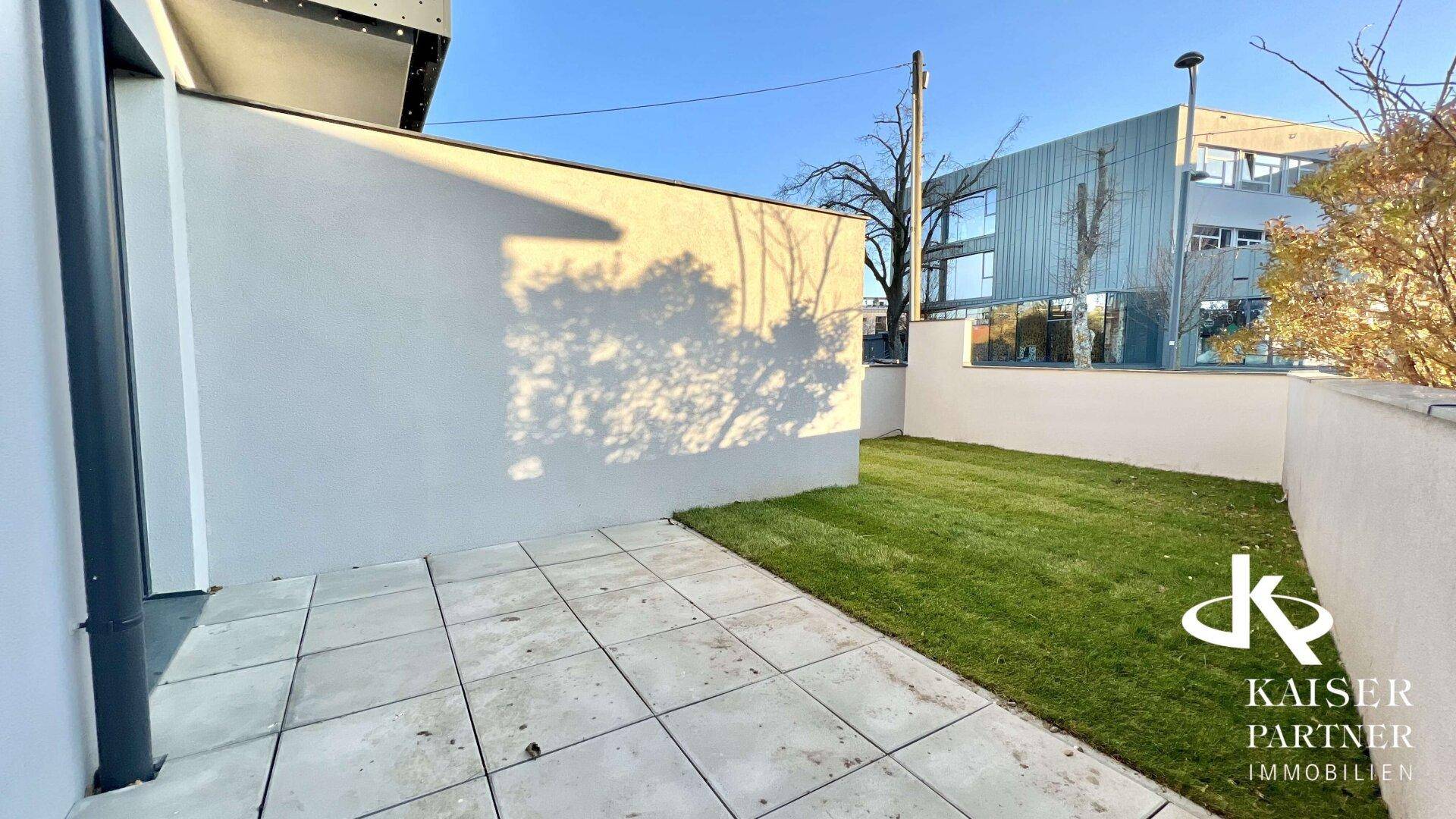 Sonniger Terrassenbereich mit Rasenfläche und moderner Architektur im Hintergrund.