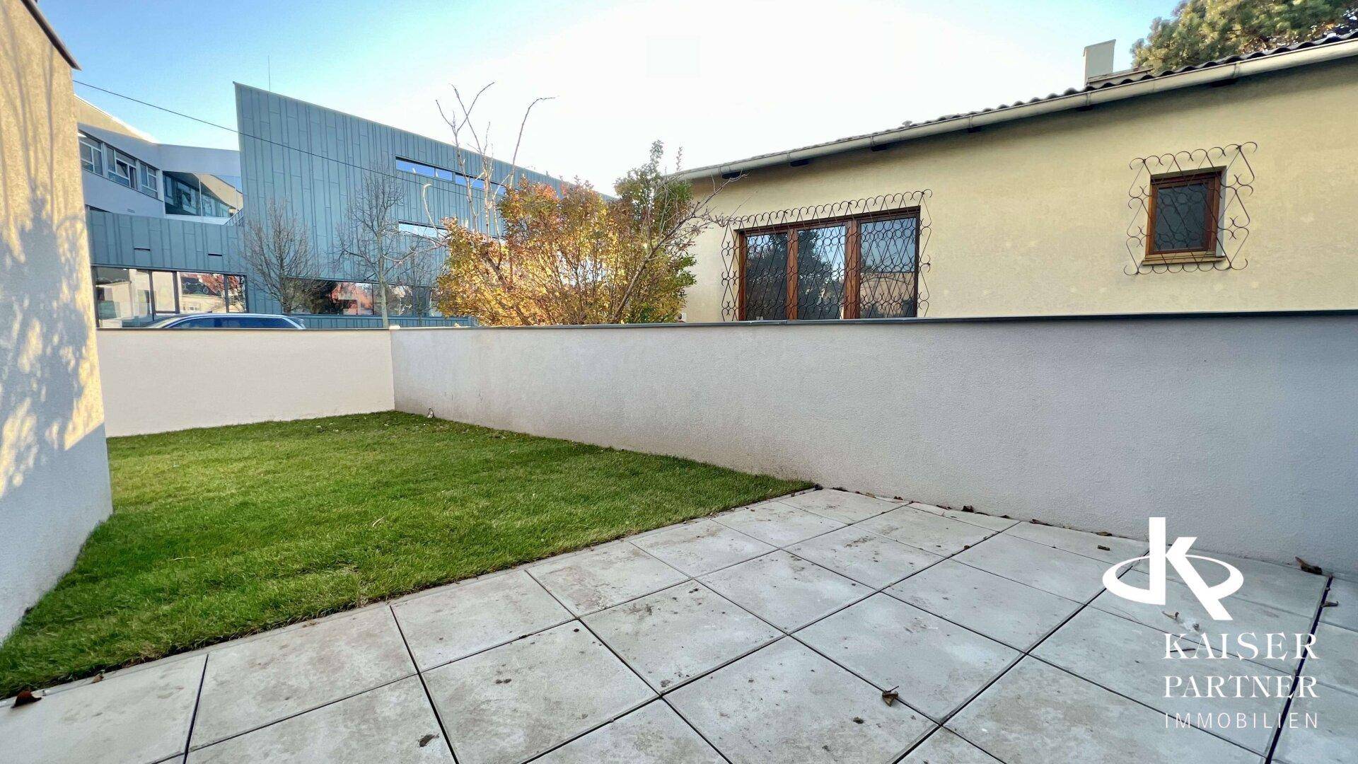 Gepflasterte Terrasse und kleiner Rasenbereich mit Blick auf die Umgebung und angrenzende Gebäude.