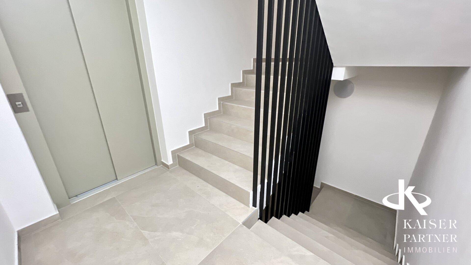 Heller Treppenaufgang mit modernem Geländer und integriertem Aufzug im Gebäude.