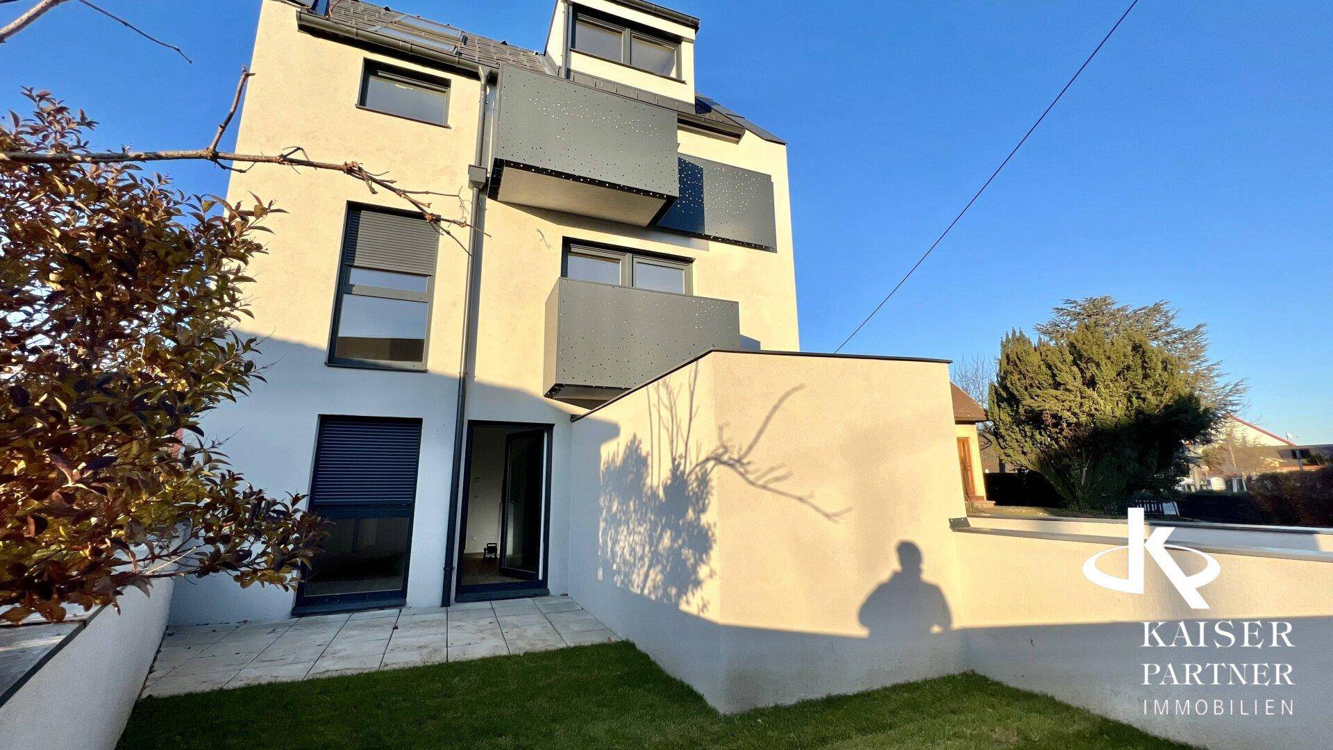 Moderne Wohnanlage mit Balkonen und privatem Gartenbereich unter strahlendem Himmel.