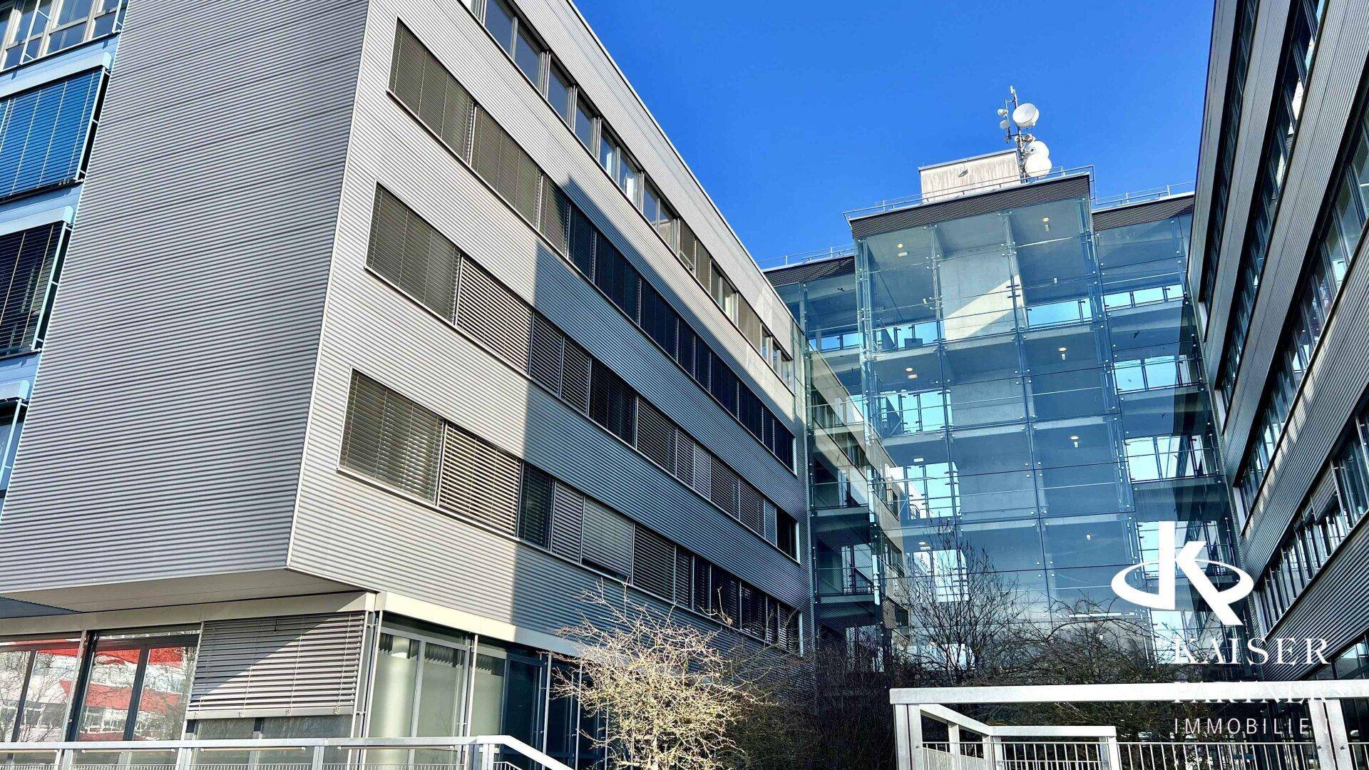 Aussenansicht des modernen Bürogebäudes mit Glas- und Metallfassade an einem klaren, sonnigen Tag.