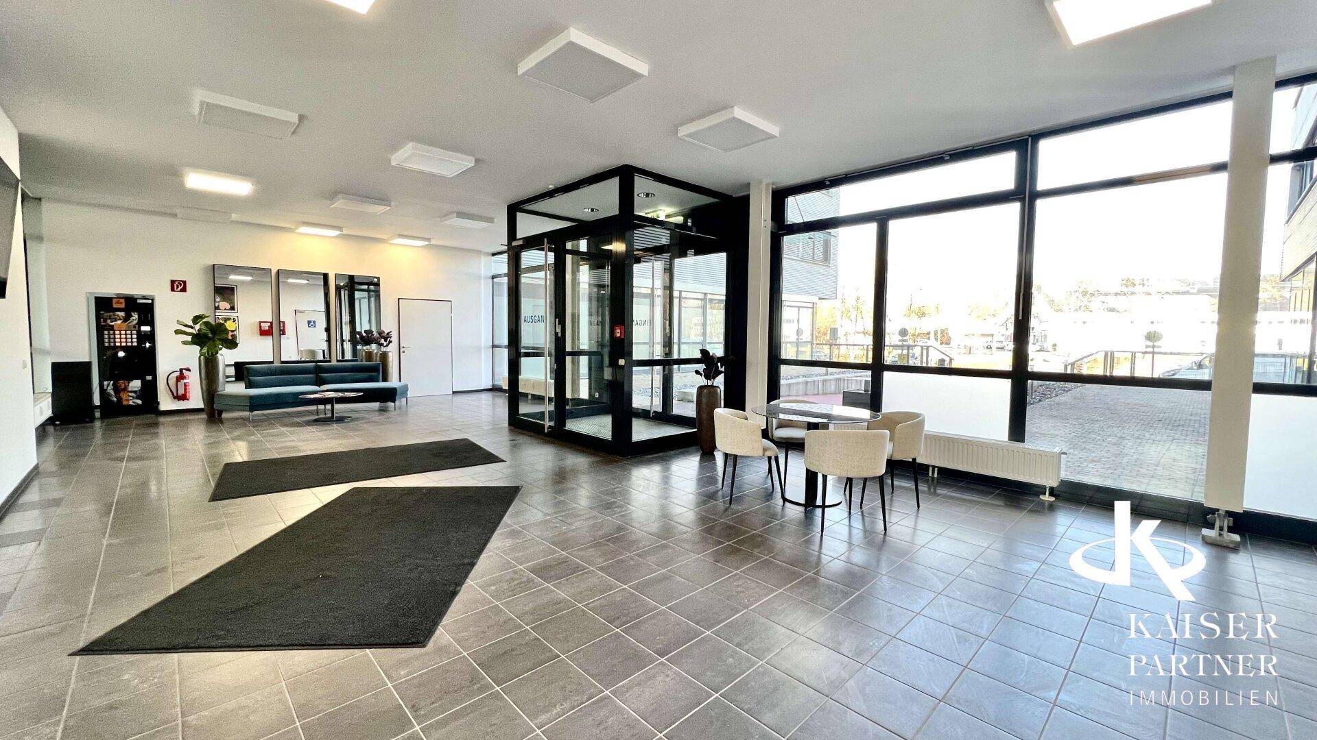 Geräumige moderne Lobby mit Fliesenboden, Sitzgelegenheiten und einem gläsernen Aufzugsbereich.