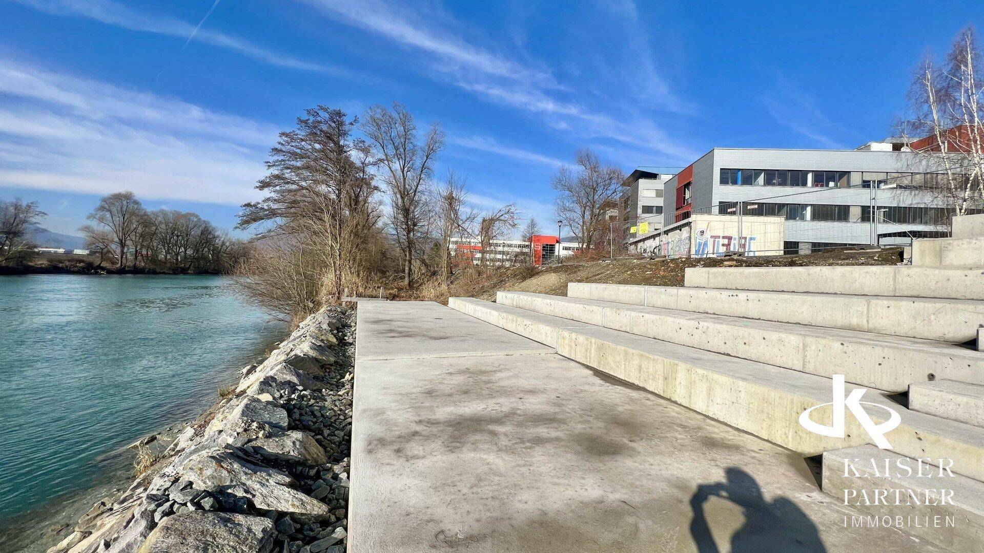 Flussufer mit Betontreppen und Blick auf die modernen Bürogebäude im Hintergrund.