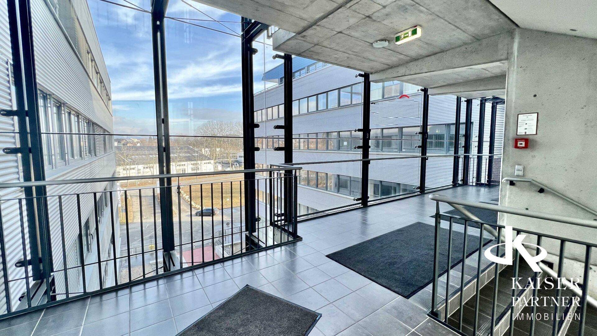 Heller Korridor mit großen Glaswänden und Blick auf die moderne Architektur des Gebäudes.