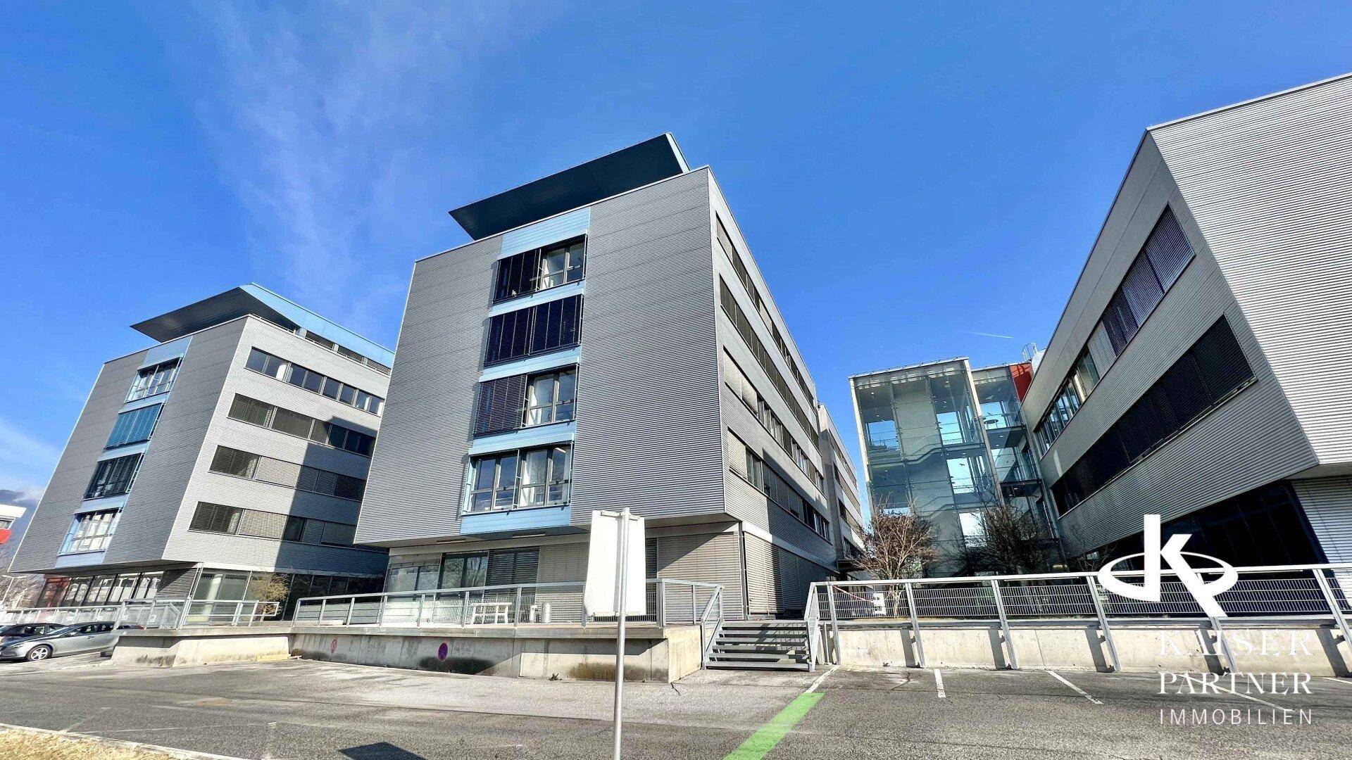 Mehrere moderne Bürogebäude mit Parkplätzen und klarem Himmel an einem sonnigen Tag.